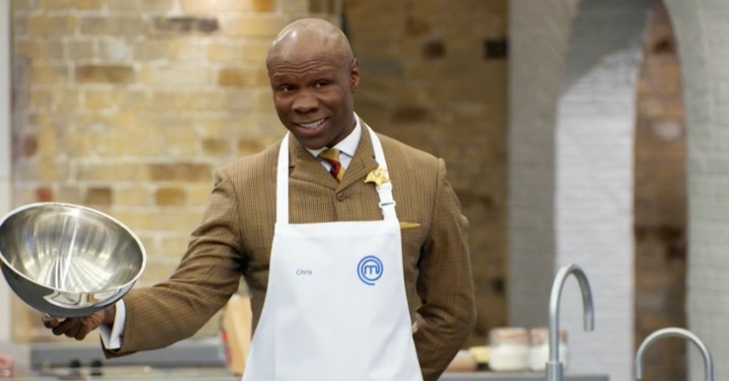 Chris Eubank wearing a brown suit and white apron lifting a cloche on Celebrity MasterChef