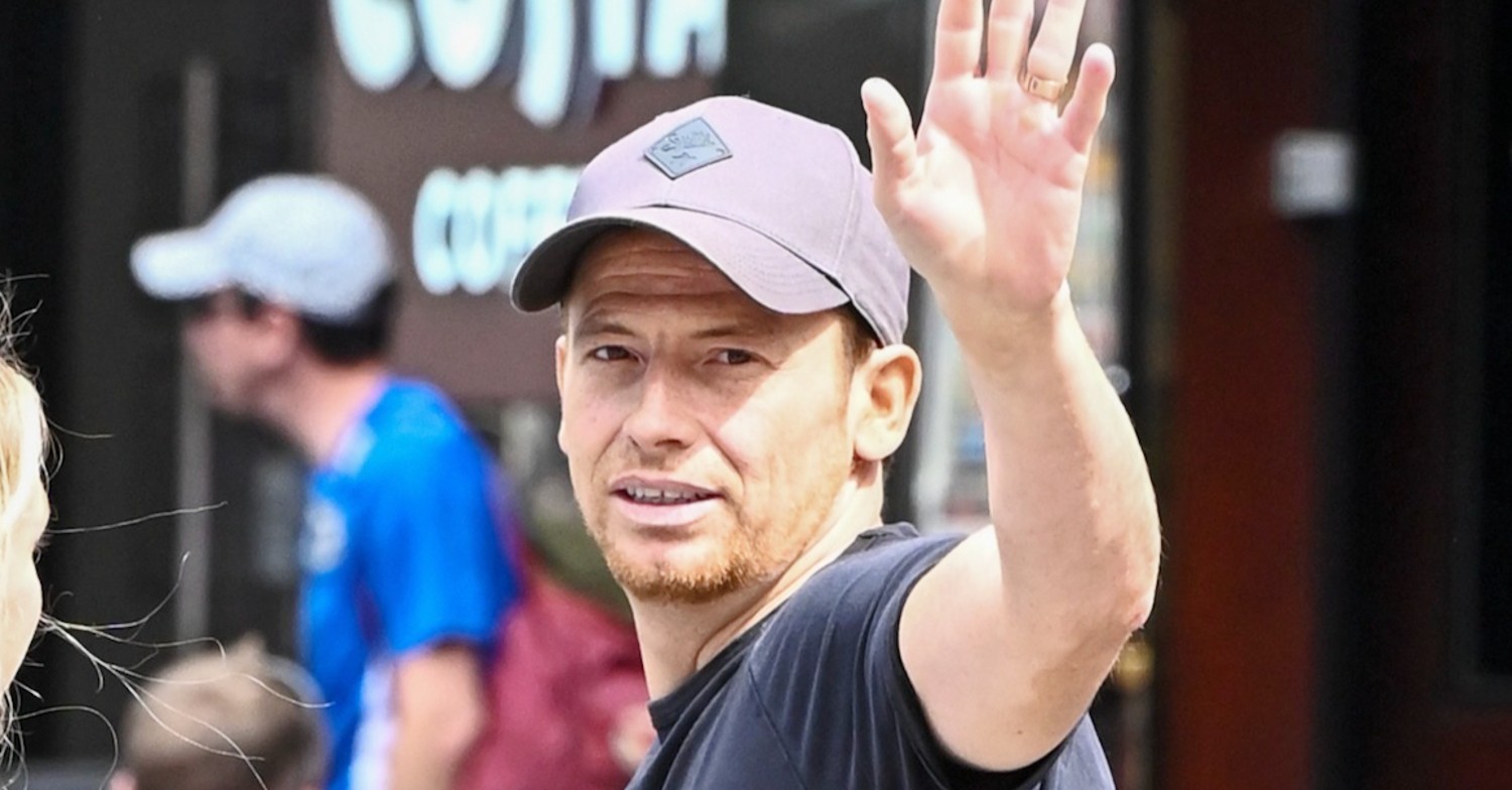 Joe Swash waves while wearing a baseball cap