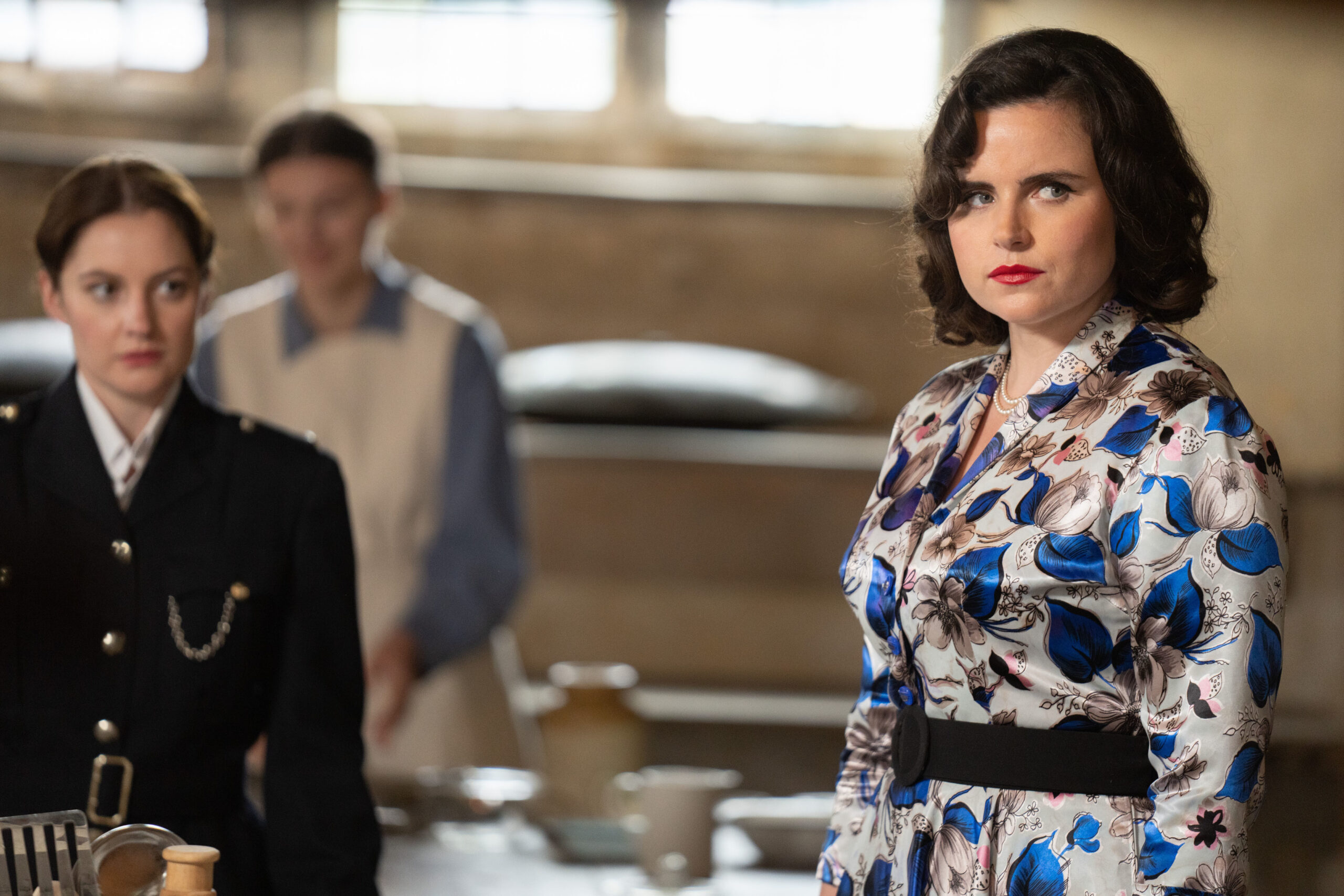 Emer Kenny as Bunty in Father Brown, she's at a party and looks angry in a blue and white dress