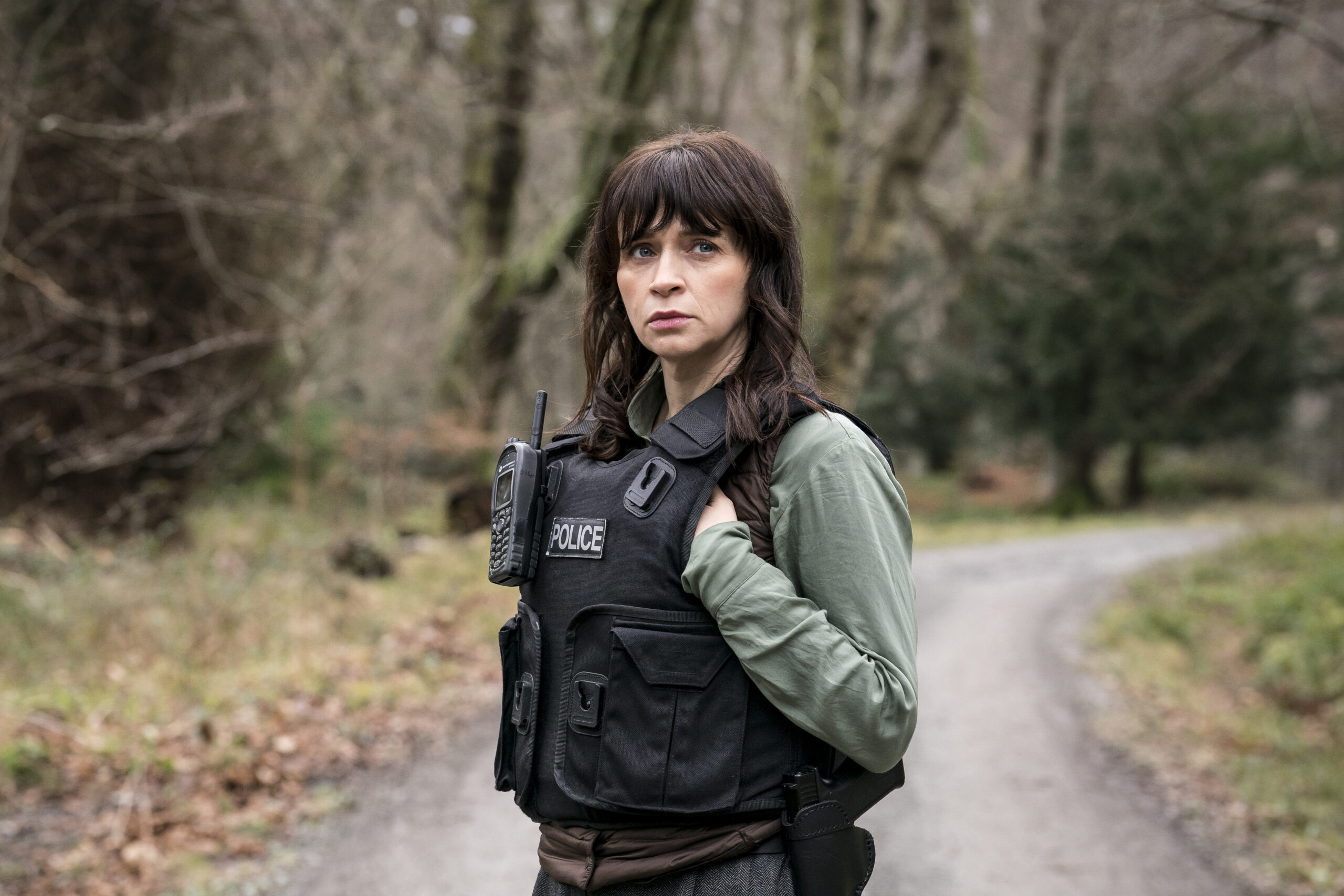 Bloodlands,First Look,Niamh McGovern (CHARLENE McKENNA) She is in the woods, with a bulletproof vest on which she holds up with a worried expression