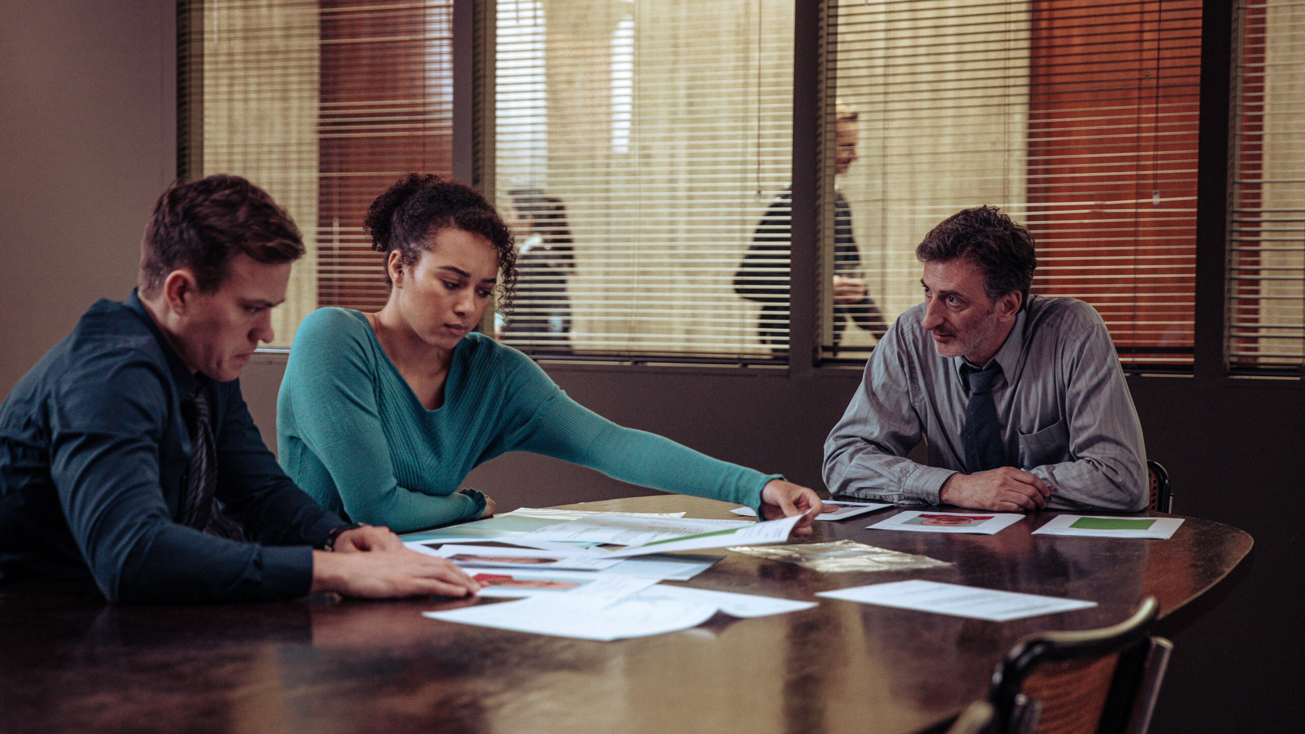 Barney White as Dan Winters (left), emma naomi as lisa donkers and andy gathergood as paul rabbit (right), they sit at a table in the jail with case notes in front of them, in Professor T series two, episode one