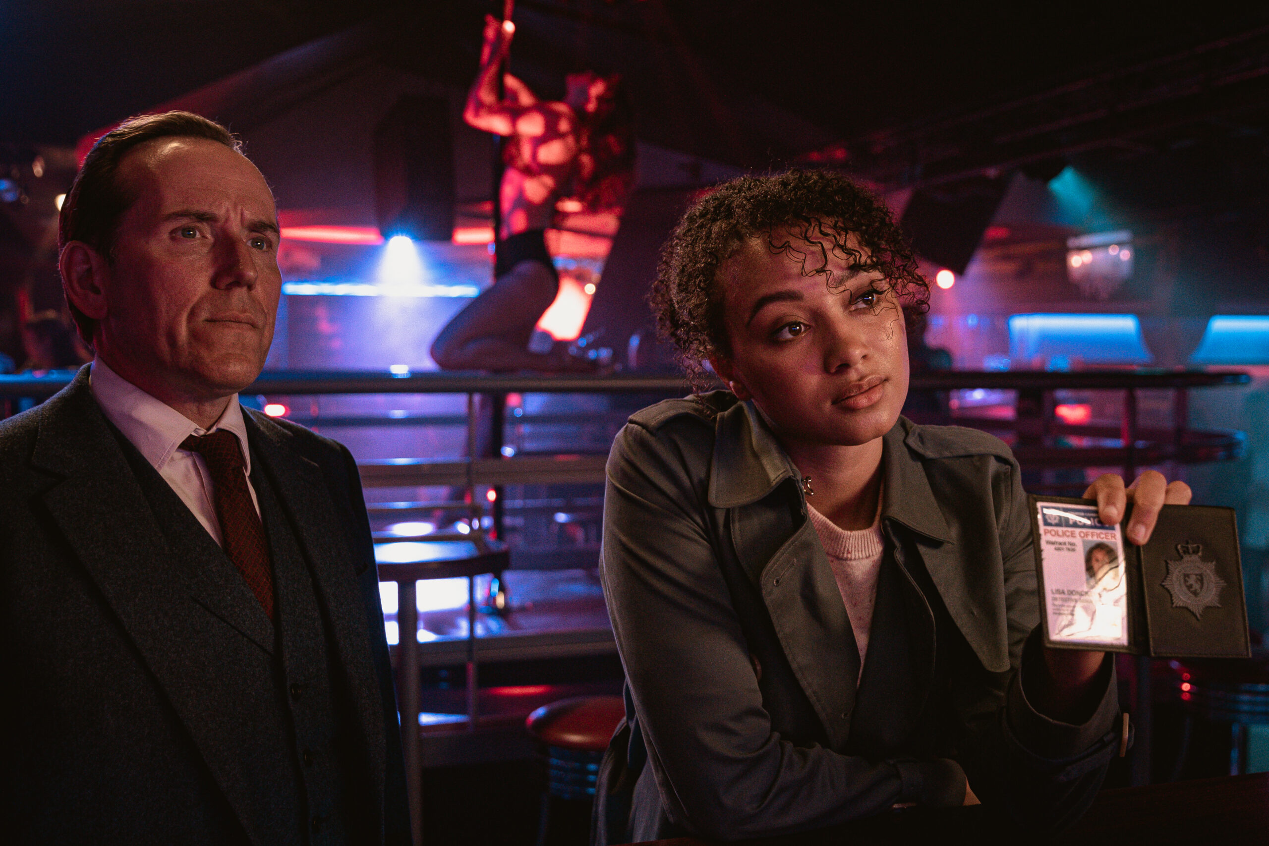 Ben Miller as Professor T and Emma Naomi as Lisa Donkers in Professor T series two, episode one, they stand in a dark venue as Lisa shows her police ID