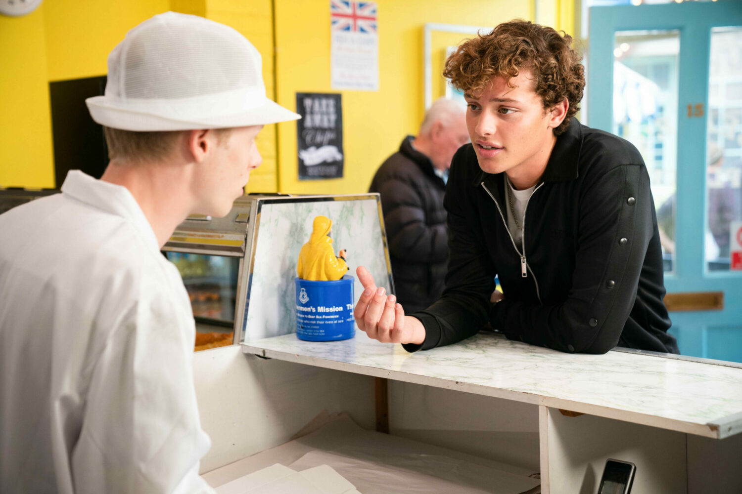 Freddie Slater leaning over the counter talking to Bobby 