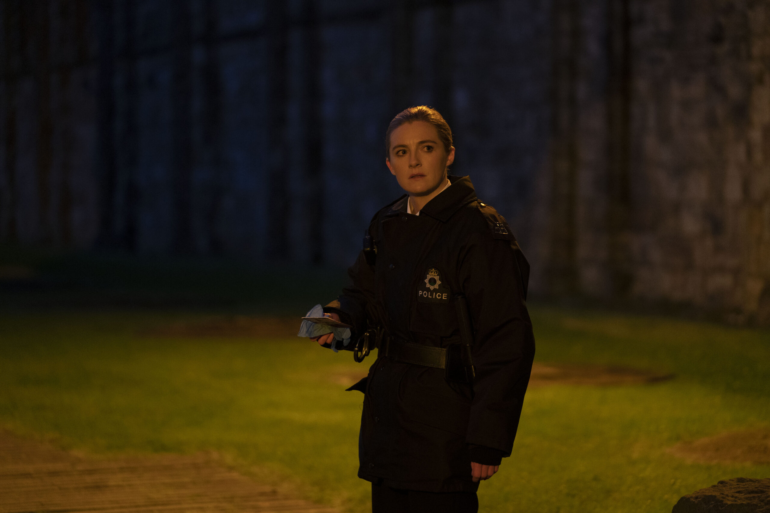 Gemma McElhinney as PC Janice Hogg, she is in her police uniform in a graveyard, holding up evidence she looks right
