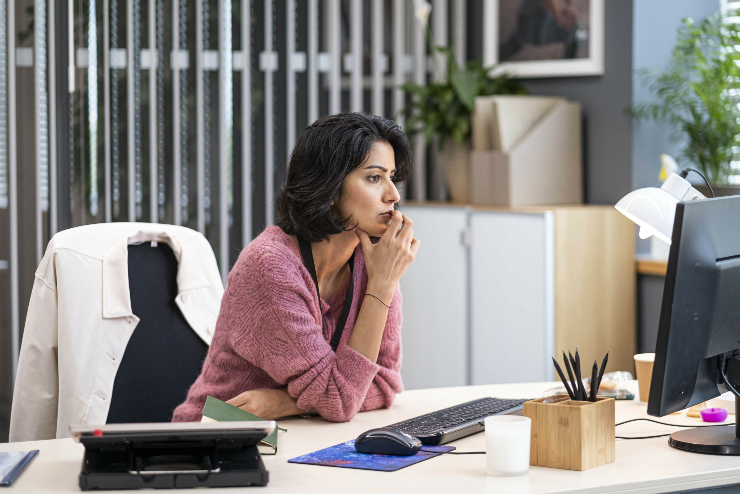 Rakhee Thakrar as Maya in Rules of the Game, she stares into a computer in a pink jumper