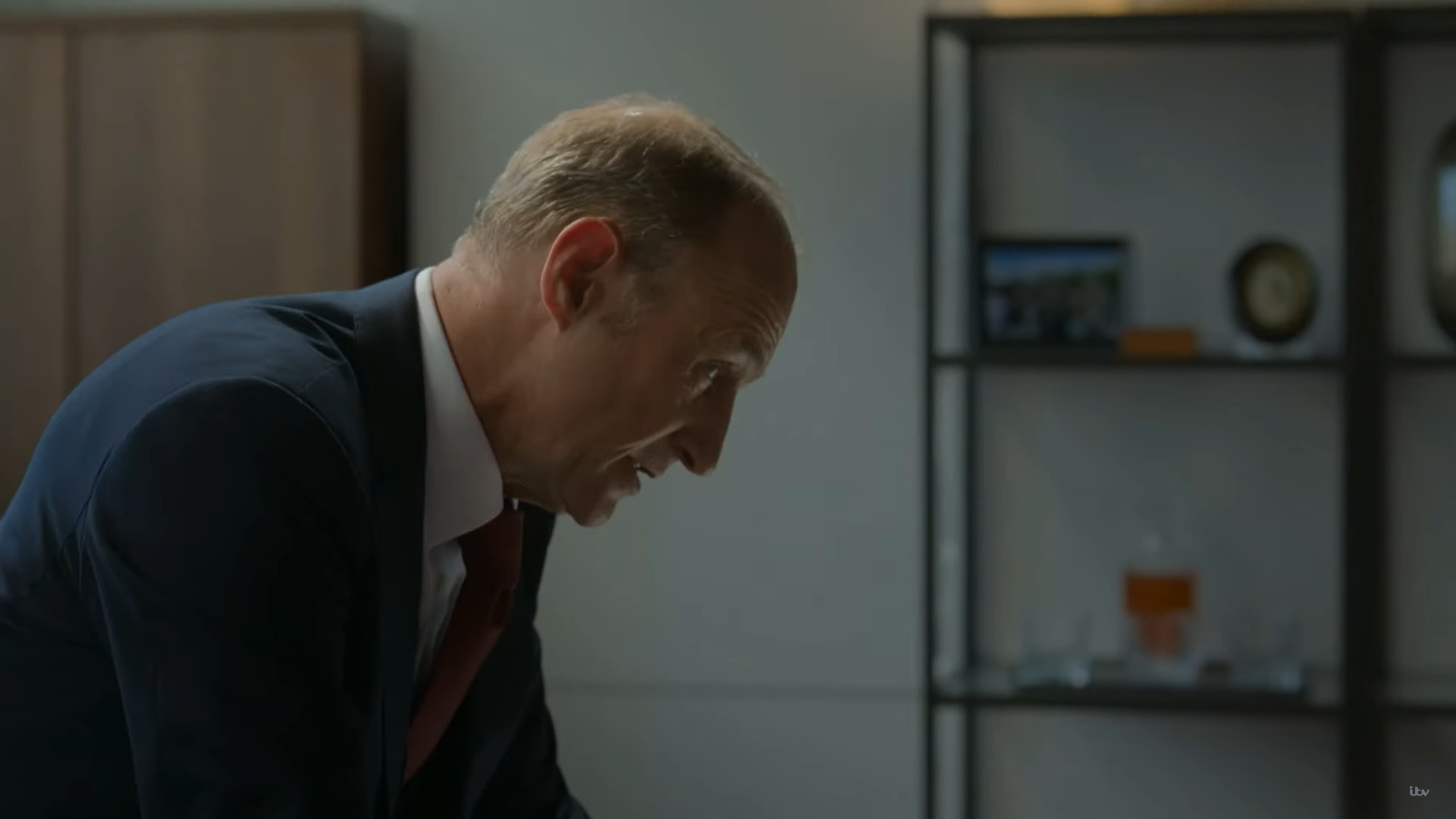Stuart Bowman as CS Lawson, he looks down at his desk in his office