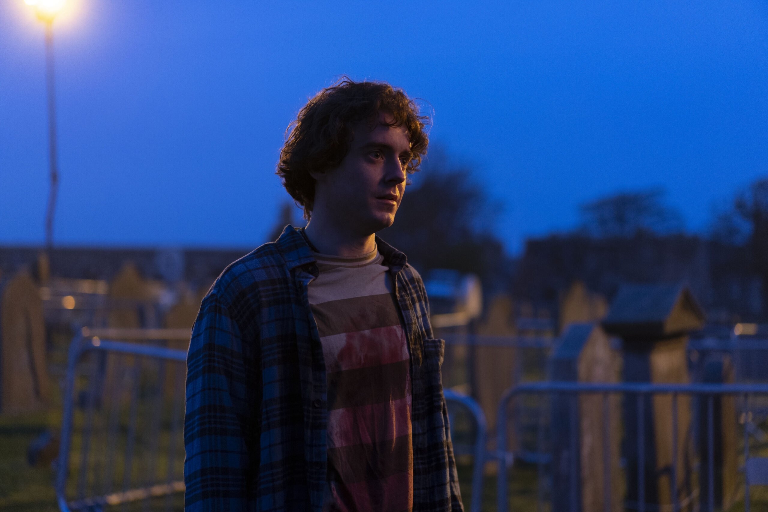 John Lumsden as Ziggy Jnr, he stands with a blood stained shirt in a dark street 