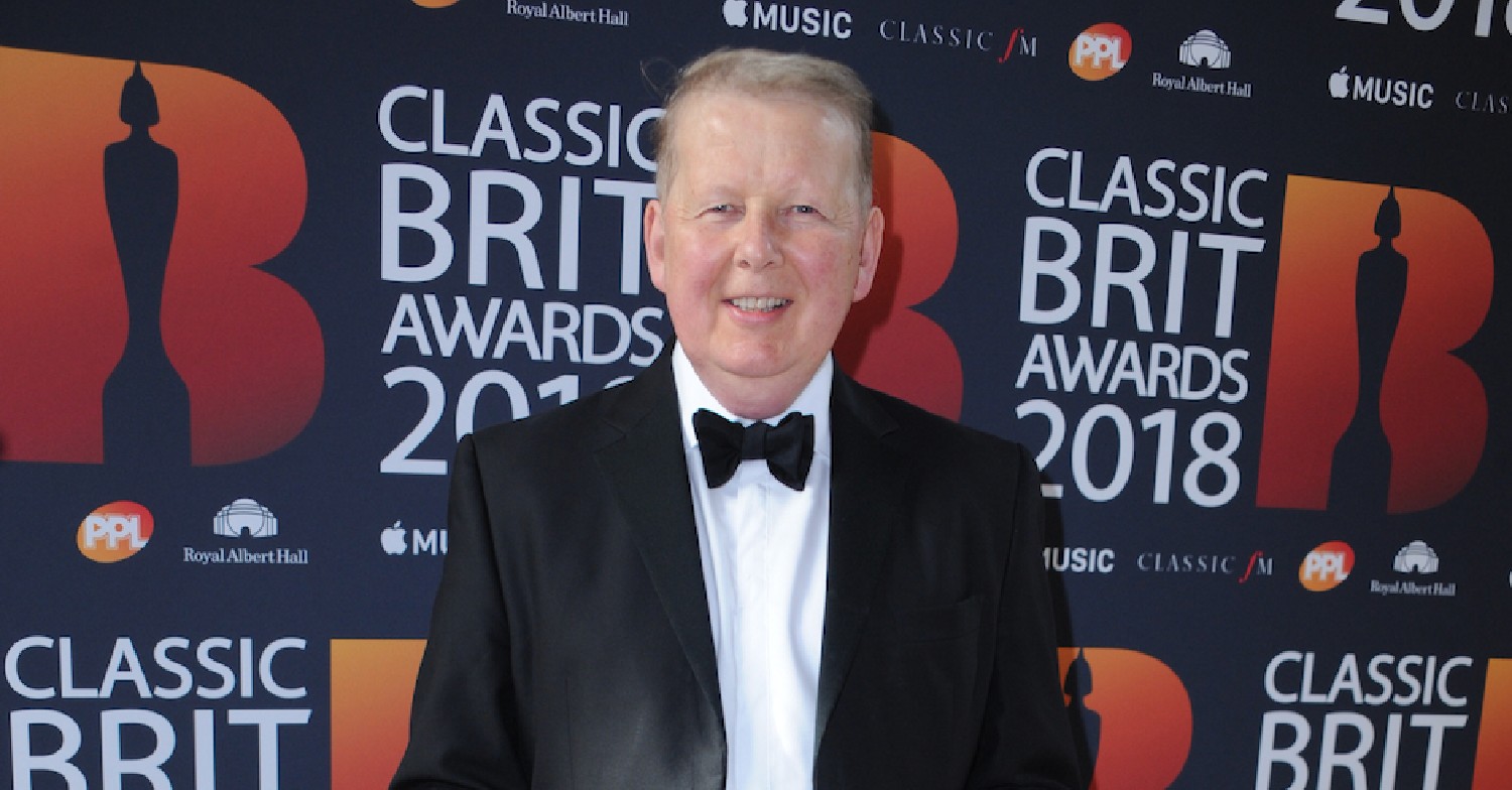 Bill Turnbull in bow-tie standing in front of Classical brit Awards board