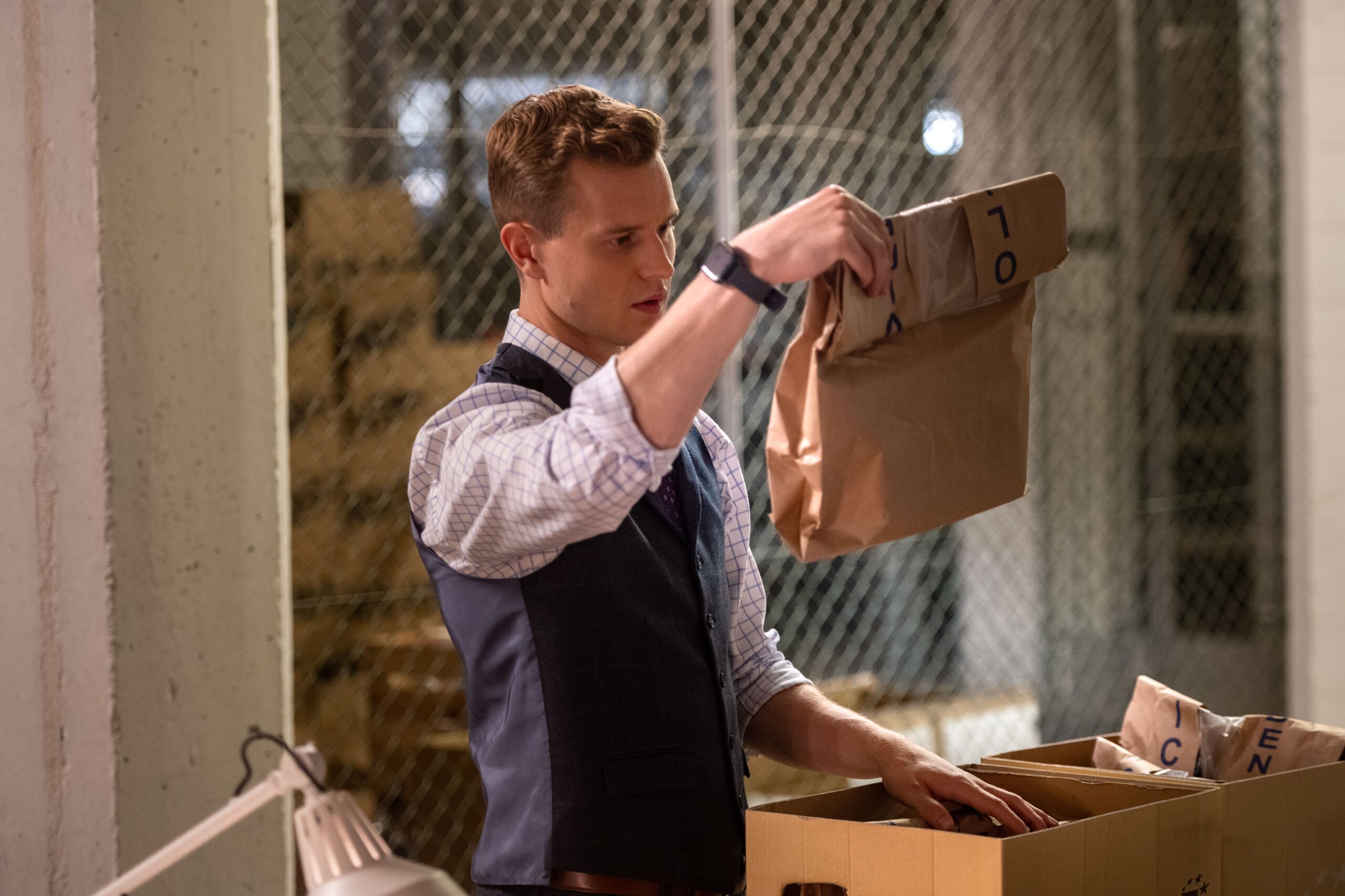 Chris Jenks as DS Jason Murray, he stands in the evidence room with a puzzled expression, holding up a brown envelope
