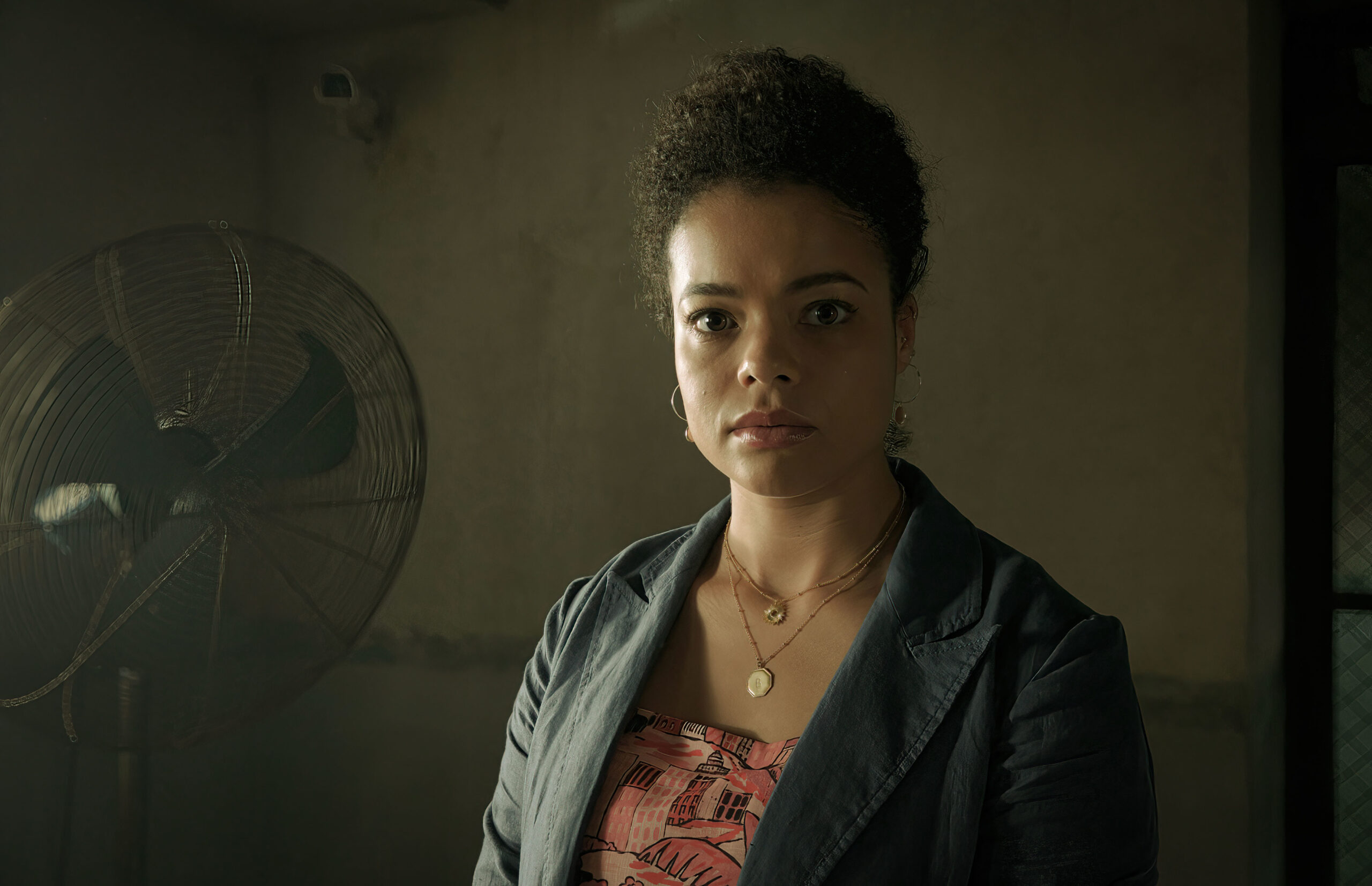 Lydia West as Beth Davenport in Inside Man, she sits in a prison room, she wears a blazer and looks into the camera with an upset expression