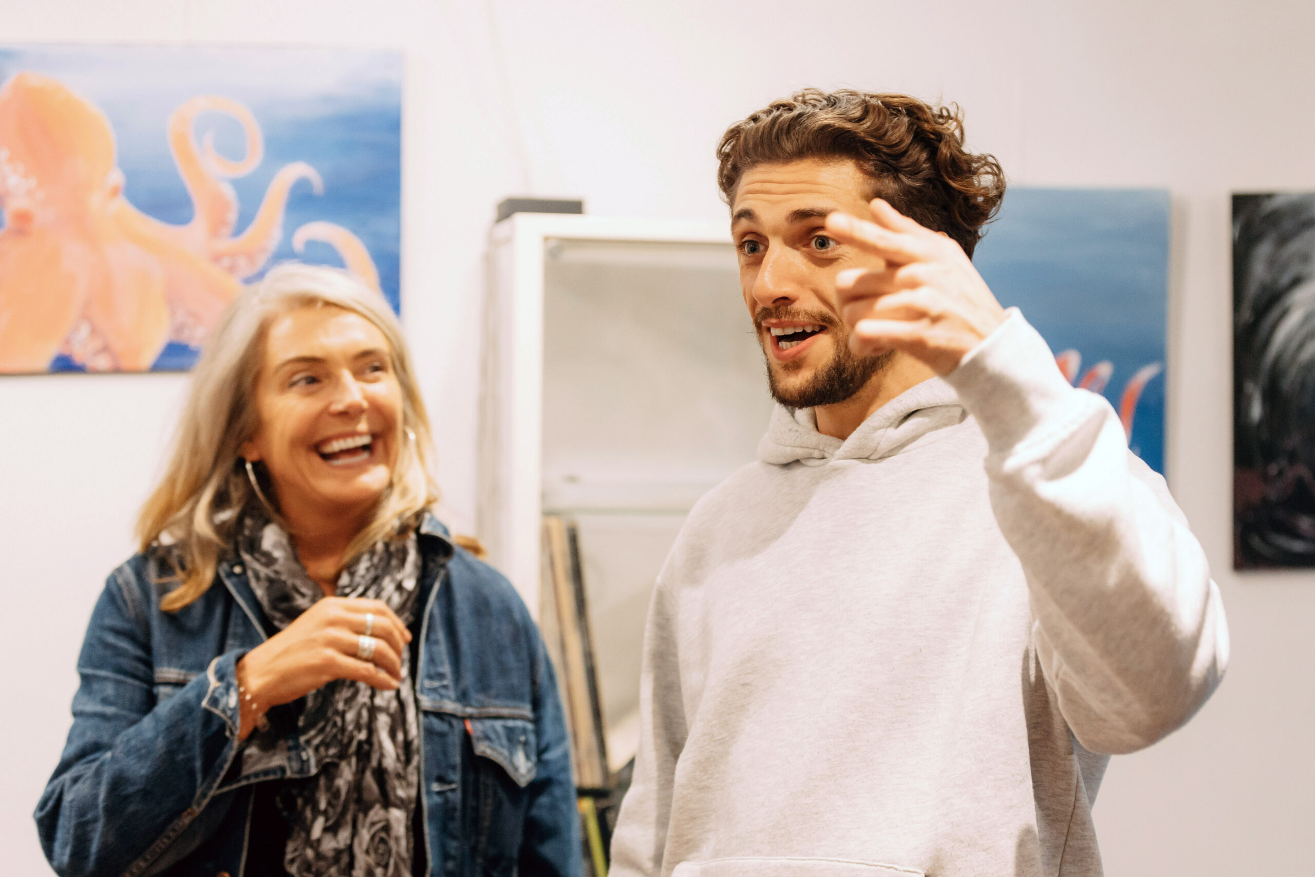 Melanie Bishop (left) and Joe Bishop (right) in Life After Deaf, they smile and laugh in art studio while Joe signs in BSL