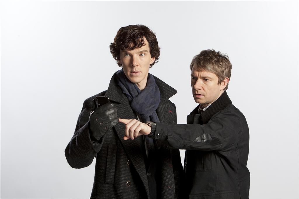 Benedict Cumberbatch as Sherlock and Martin Freeman as Watson, they stand next to eachother in black coats as Watson points in the distance