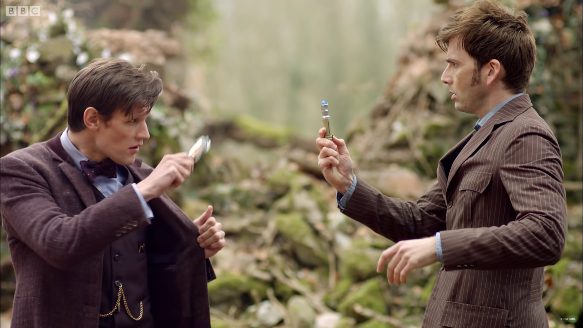 Matt Smith as The Doctor (left) and David Tennant (The Doctor) (RIGHT), they stand outside pointing sonic screwdrivers at each other wearing suits and making confused expressions