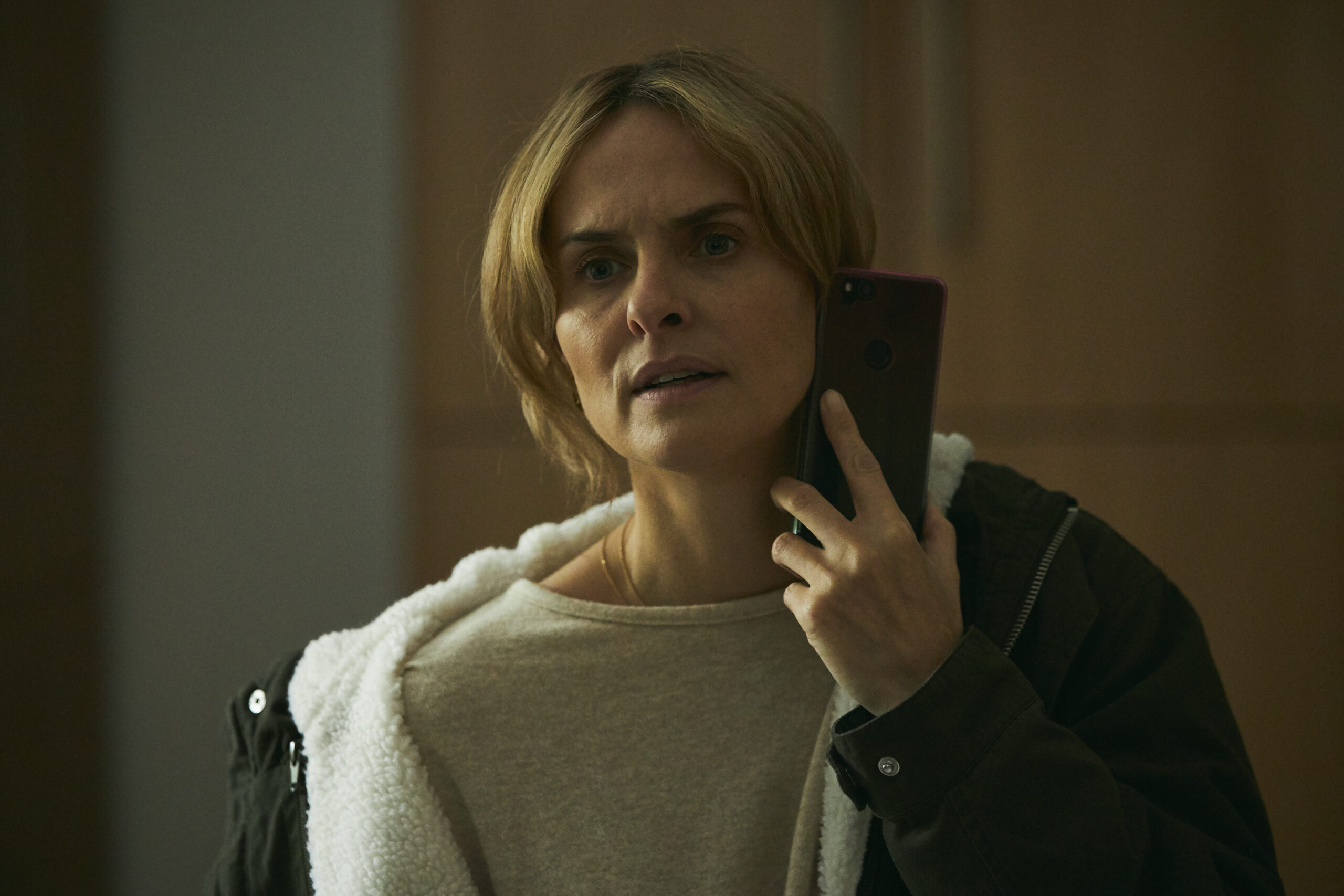 Leanne Best as Alison, she stands in a room with a coat on, she looks stressed as she's on the phone