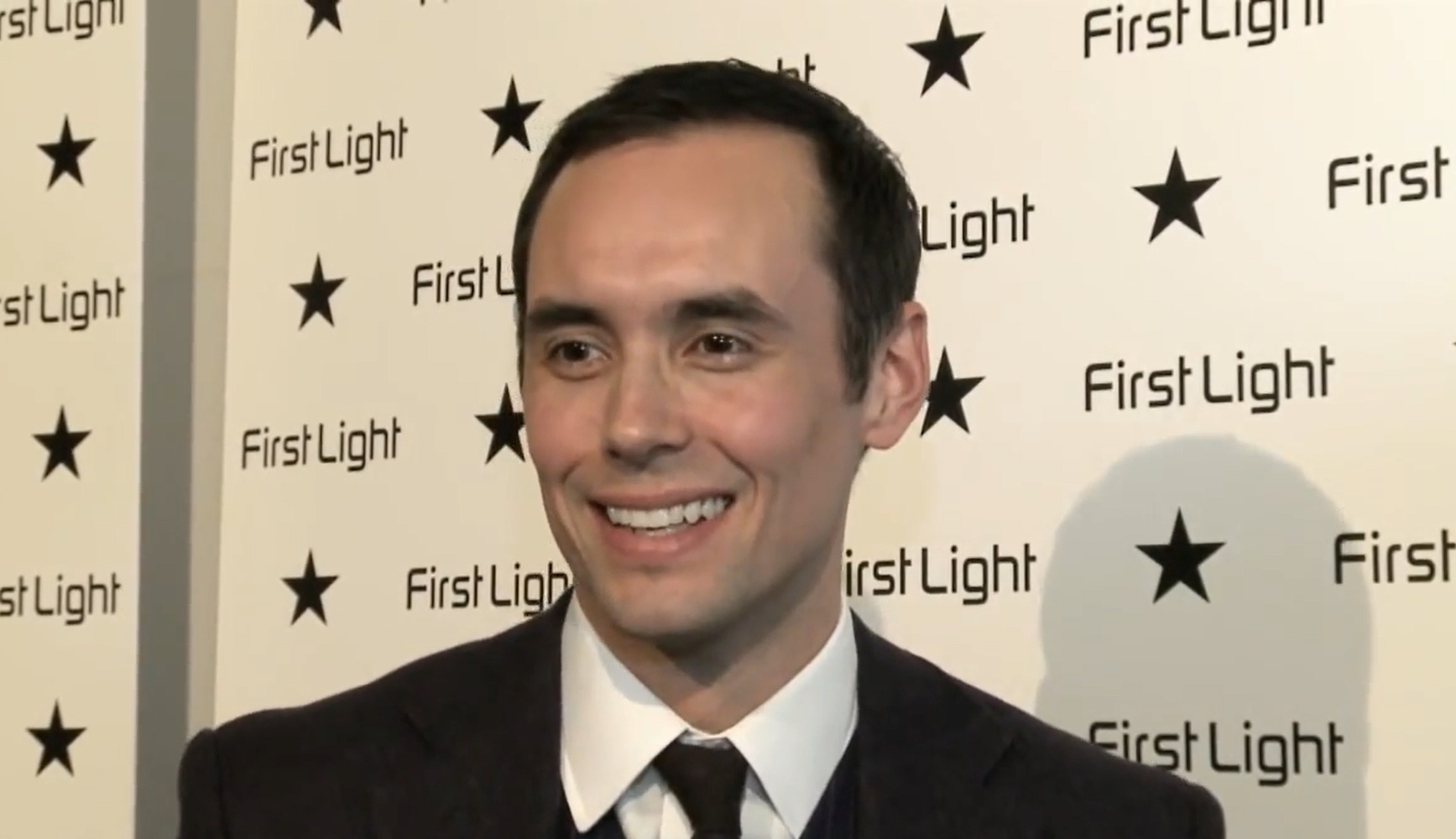 Steve John Shepherd in an interview, he at an awards show and smiles at the camera in a black suit