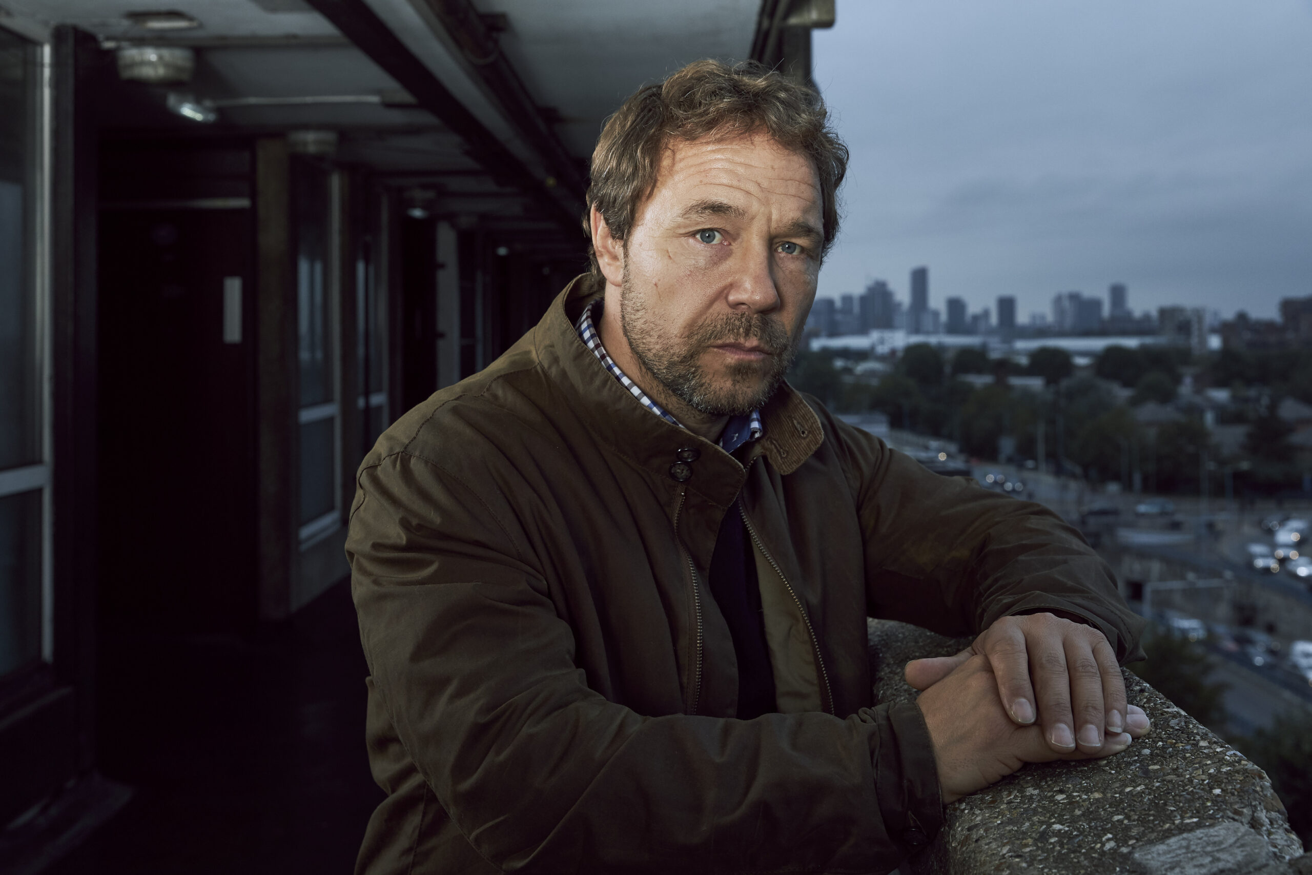 Stephen Graham as Matthew Collins in The Walk-in, he looks into the camera with a serious expression as he overlooks the London skyline