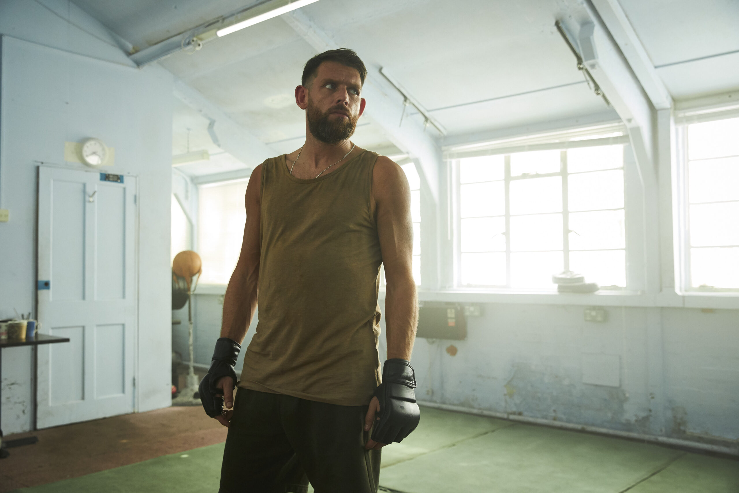 Chris Coghill as Chris Lythgoe in The Walk-In, he has boxing gloves on in a room with windows, he looks rough