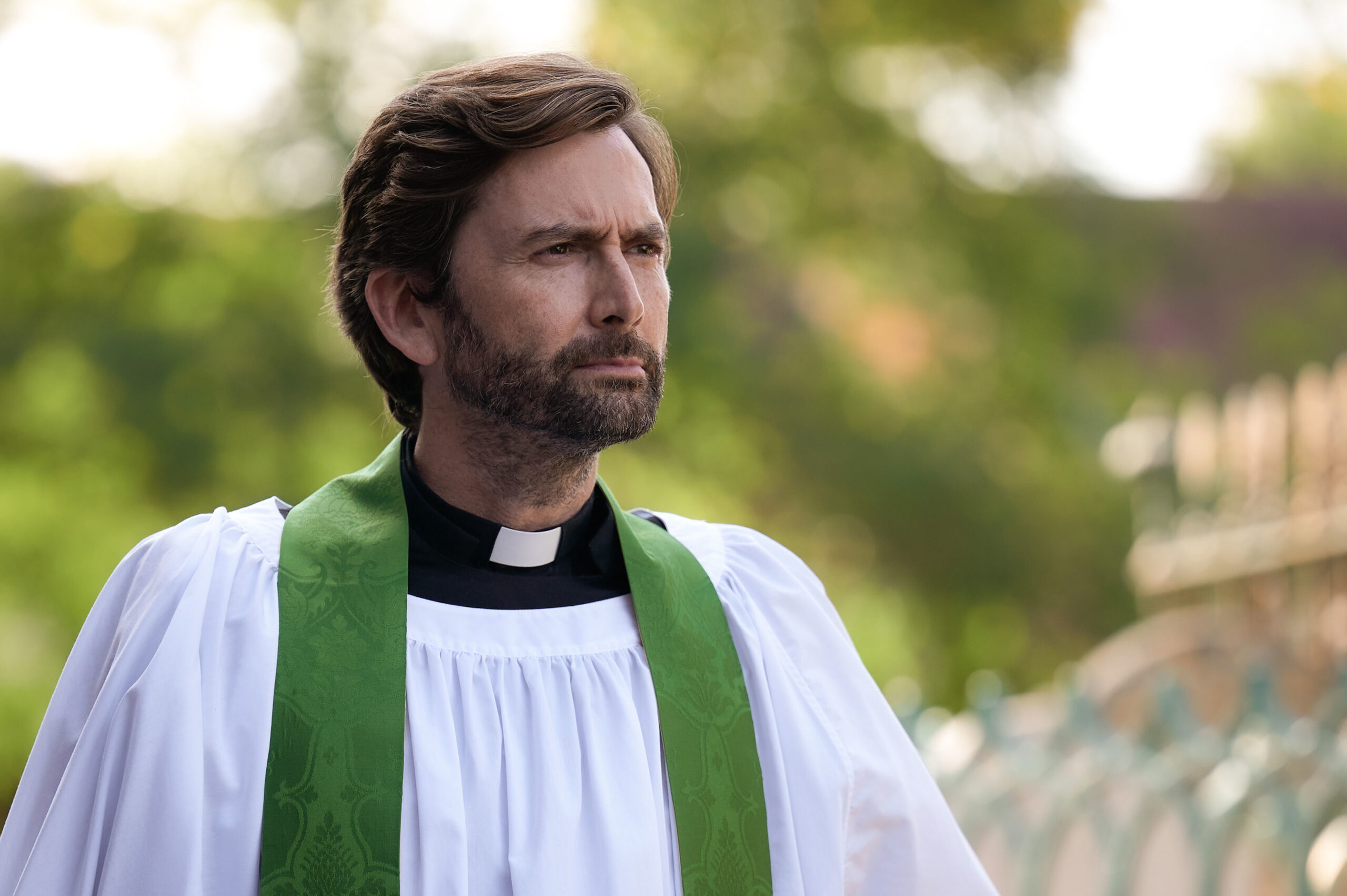 David Tennant as Henry Watling in Inside Man, he is outside in his Vicar uniform as he looks off to the right