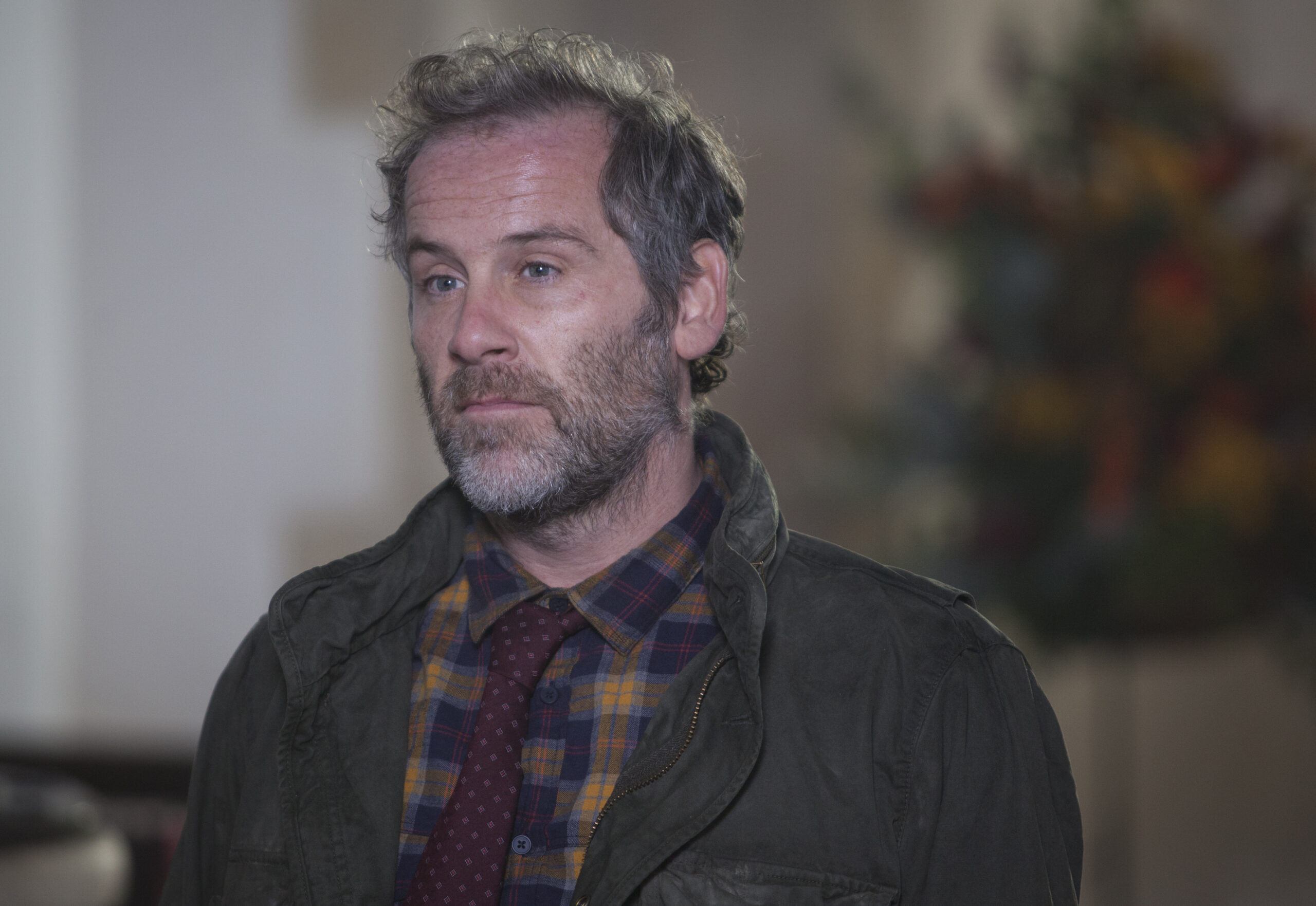 Jason Thorpe as Jimmy in Agatha Raisin, he looks to the left with a frown as he stands in front of flowers