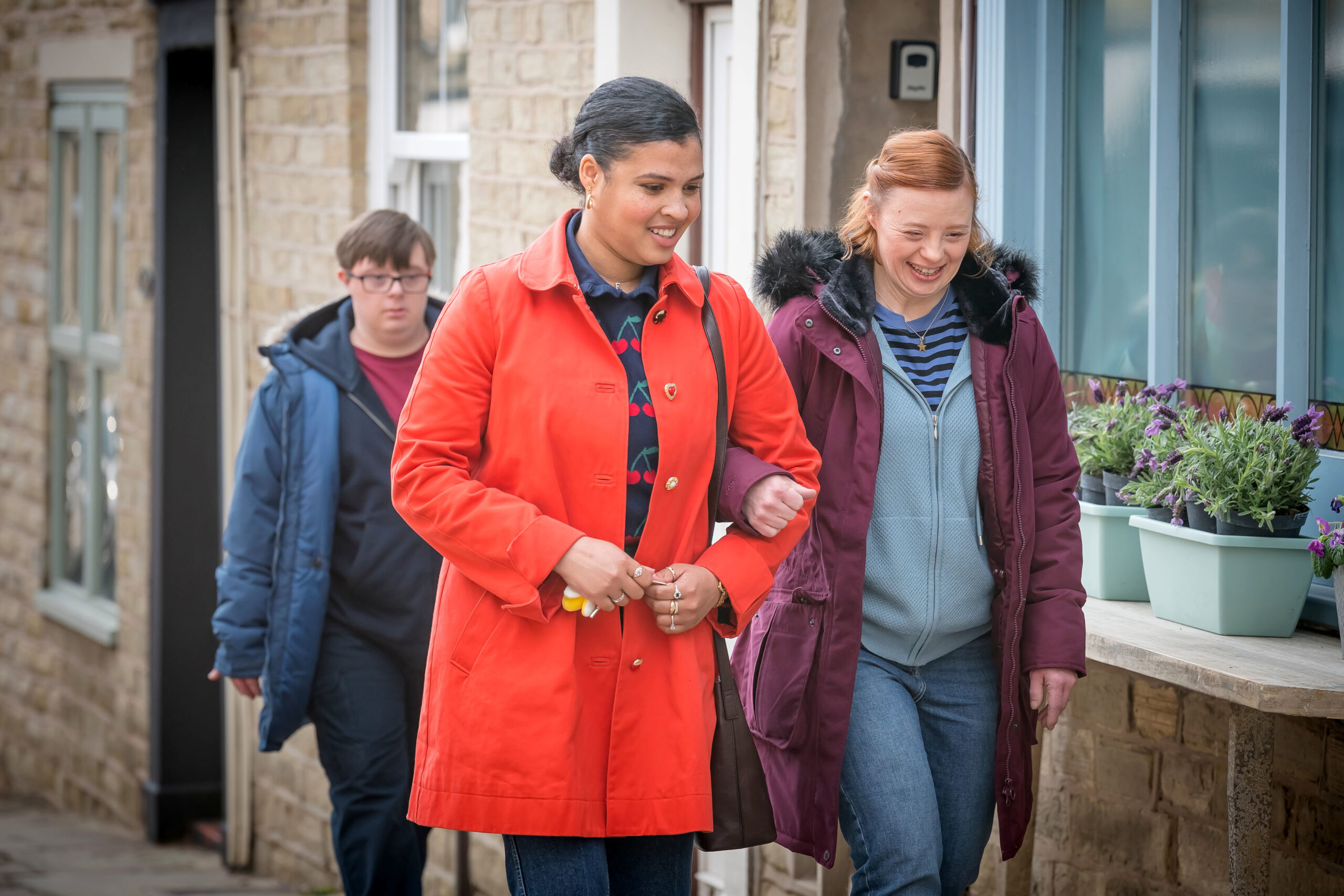 Emma (JAMIE MARIE LEARY) and Katie Wilson (SARAH GORDY) walk smiling as Ralph Wilson (LEON HARROP) follows looking more serious