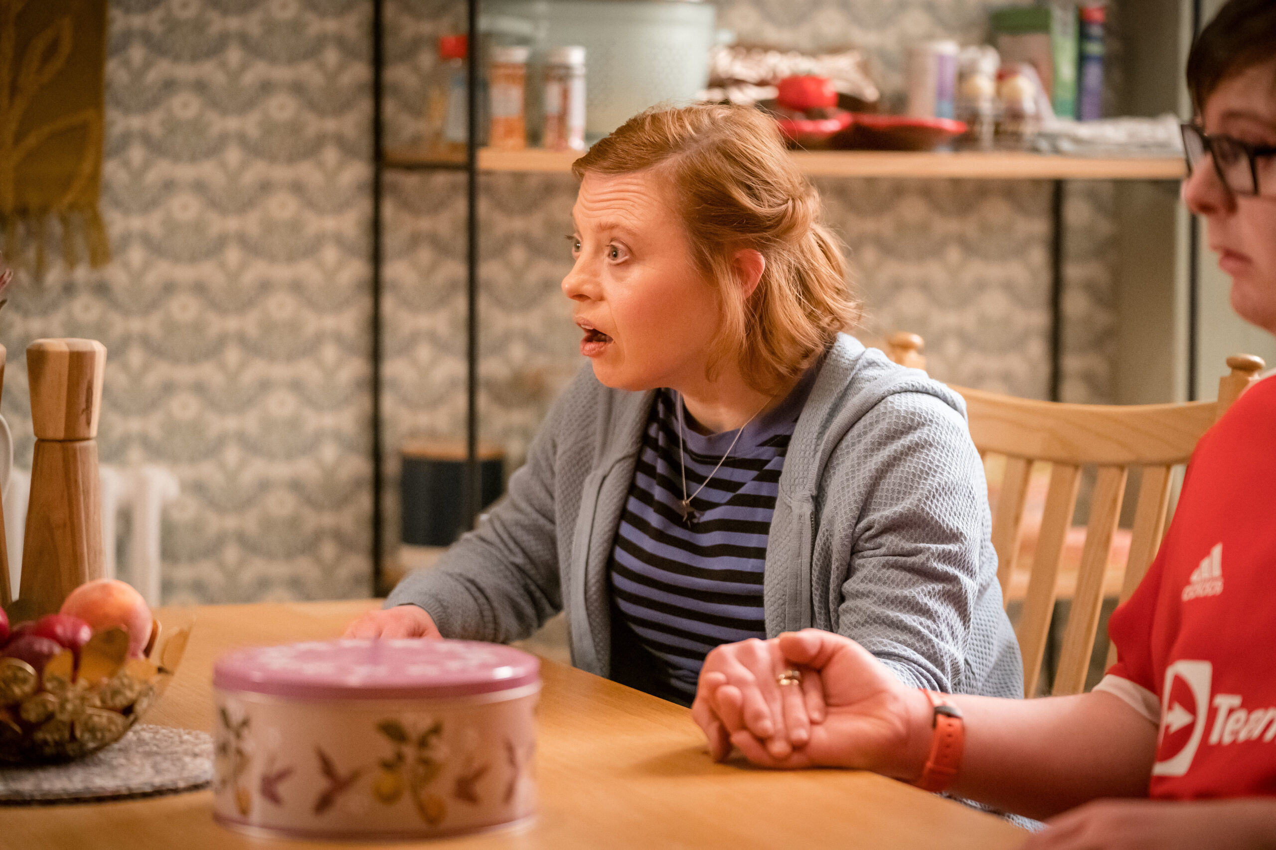 Sarah Gordy as Katie Thorne in Ralph & Katie, she sits a table with a shocked expression looking to her left