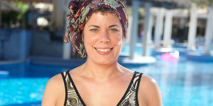 Selina Griffiths as Pauline in Benidorm, she smiles outside a pool with a swimsuit on