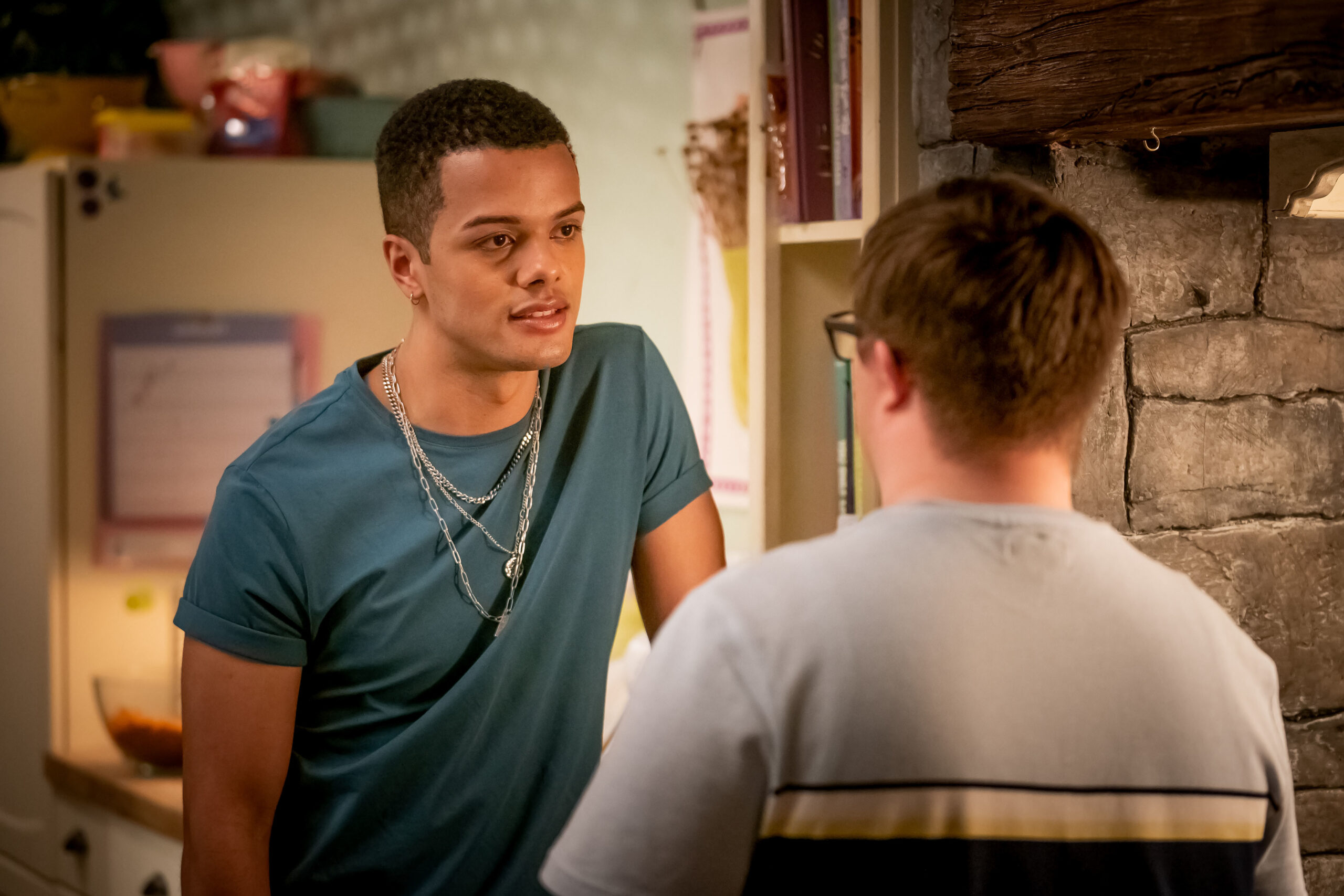 Dylan Brady as Danny in Ralph & Katie, he looks at Ralph with a smile as he leans on a counter