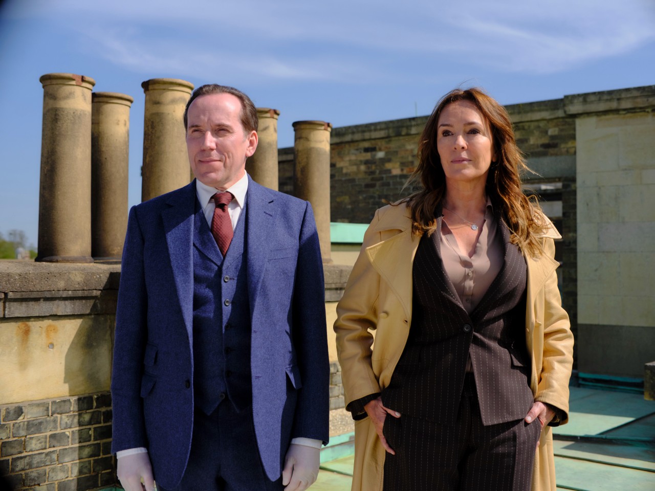 Ben Miller as Professor T (left) and Juliet Aubrey as Christina (left), they stand next to eachother on a roof with neutral facial expressions