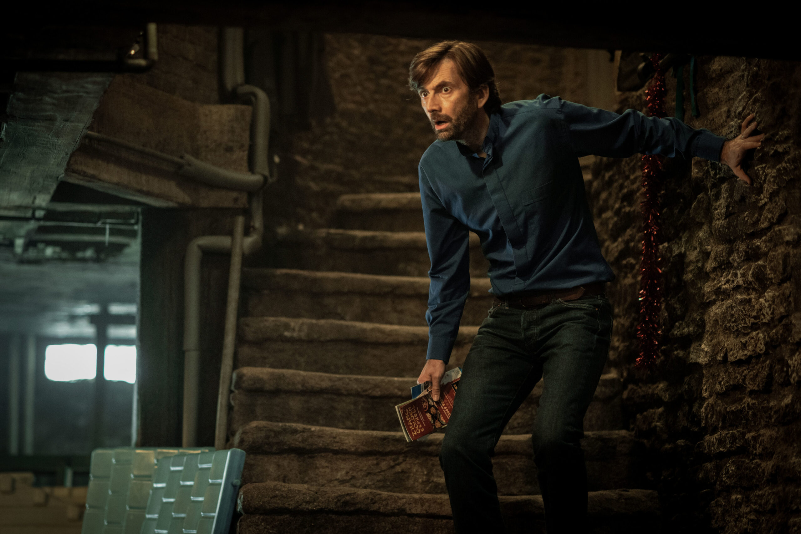 David Tennant as Henry Watling, he comes down the stairs of the cellar with a worried expression