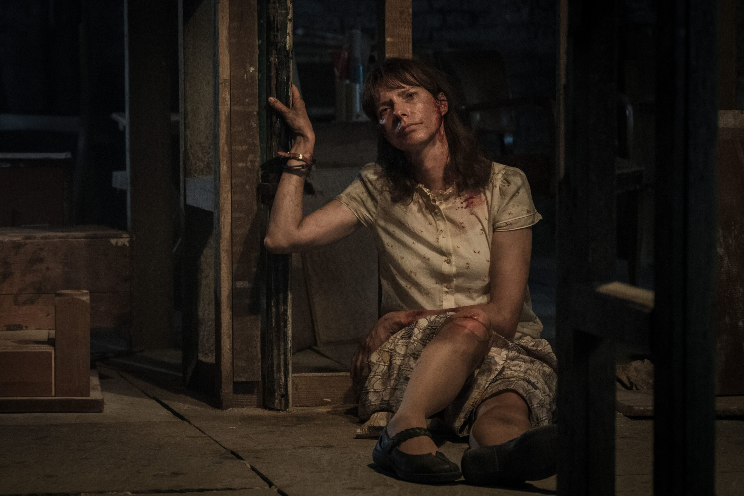 Dolly Wells as Janice Fife in Inside Man, she is in pain and looks sad as she sits on the cellar floor in a white dress