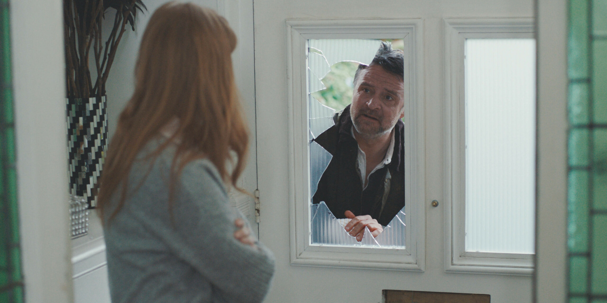 Jonty looking at Sian through a broken glass panel Casualty