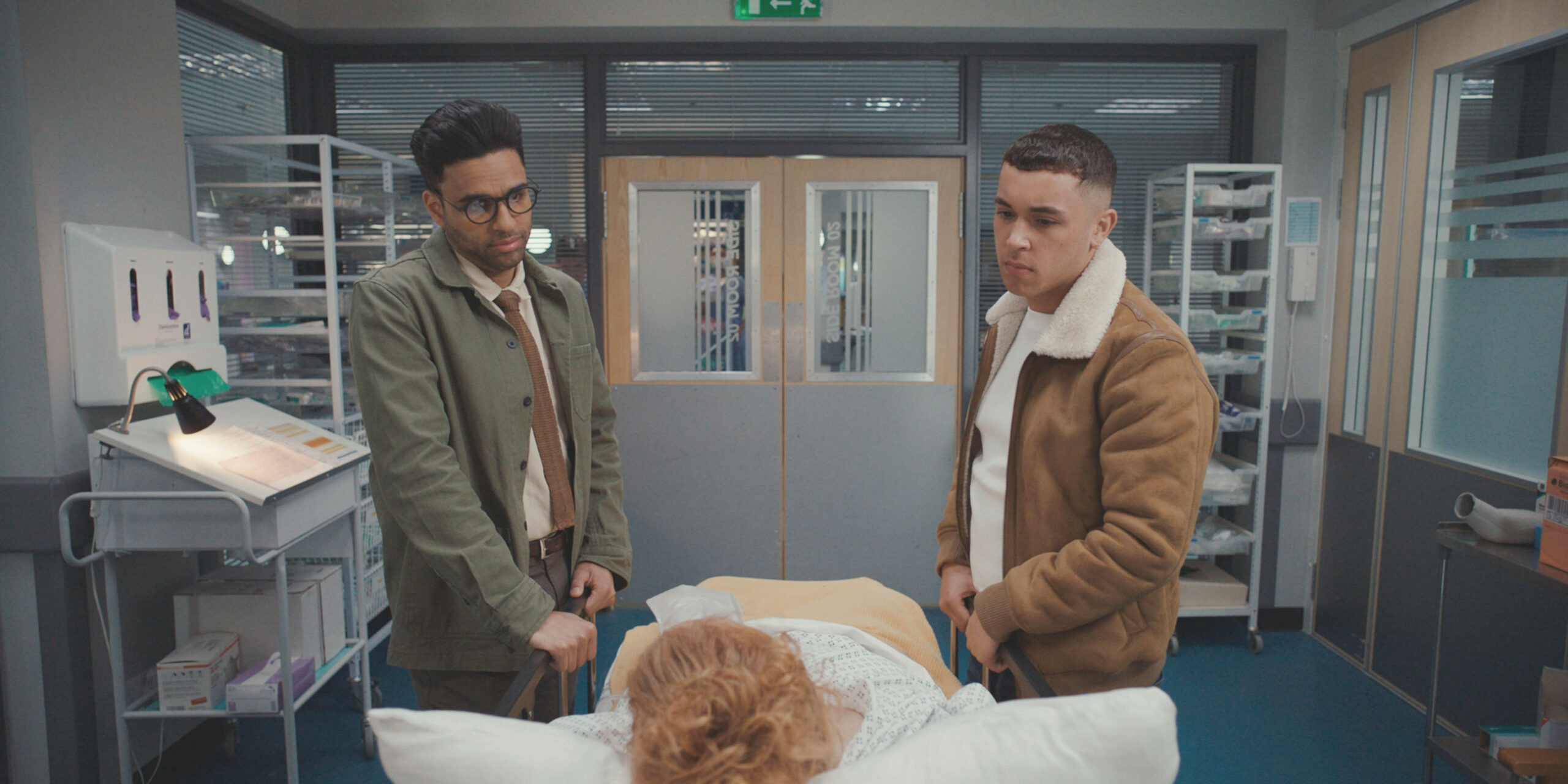Adi and Marty look at Robyn in a hospital bed Casualty 