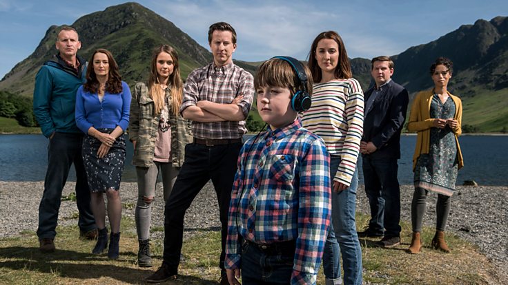 The cast of The A Word stand on a beach as they all smile into the camera