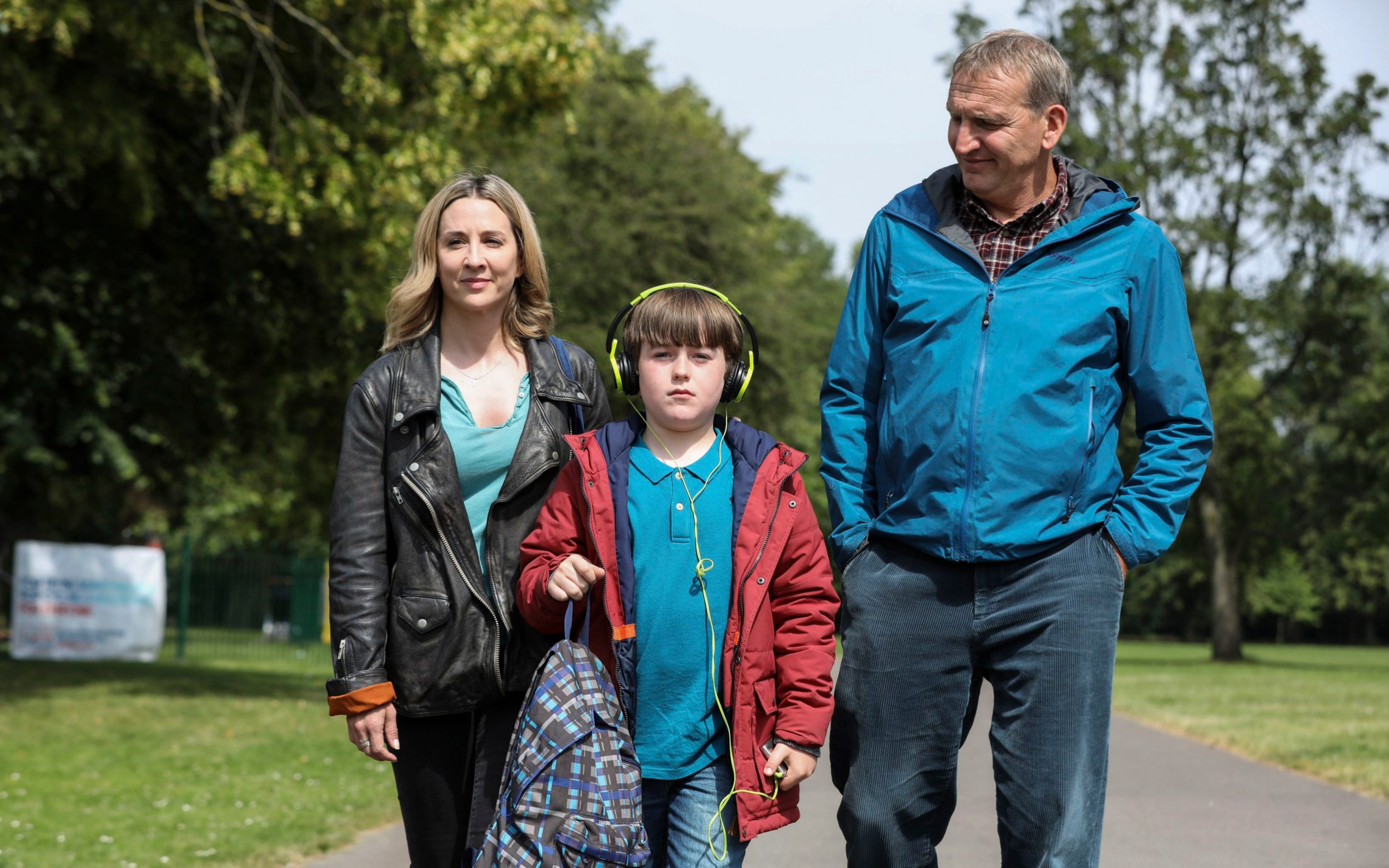 Morven Christie as Alison, Max Vento as Joe and Christopher Eccleston as Maurice in the a word, they stand outside in a park as they walk together, smiling