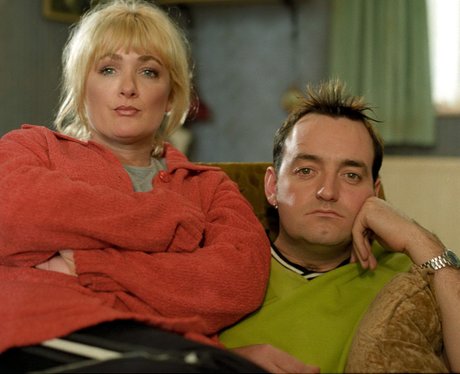 Craig Cash as Dave Best and Caroline Aherne as Denise Best in The Royle Family, they sit together on a sofa with frowns on their faces