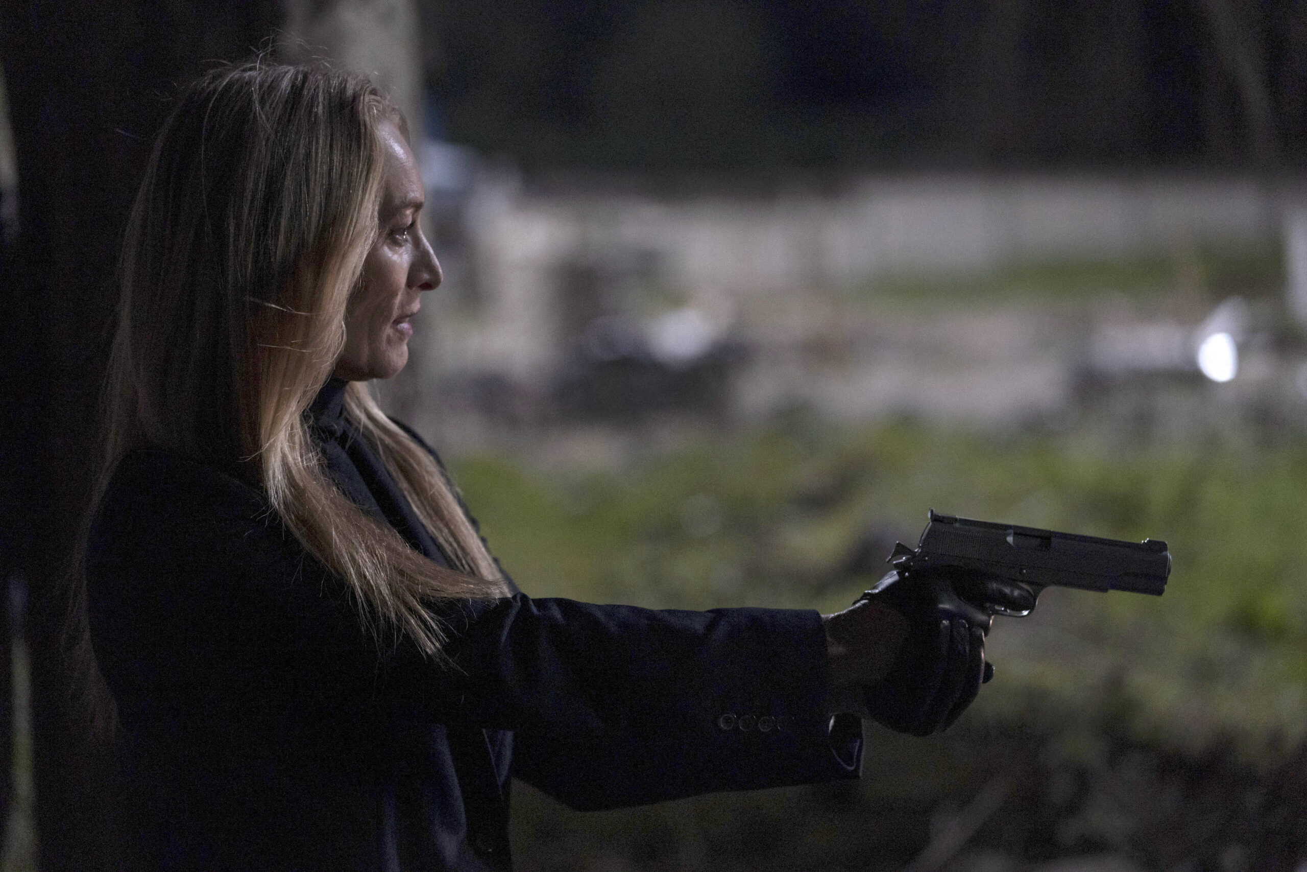 Victoria Smurfit as Olivia Foyle, she holds a gun and points it to her right