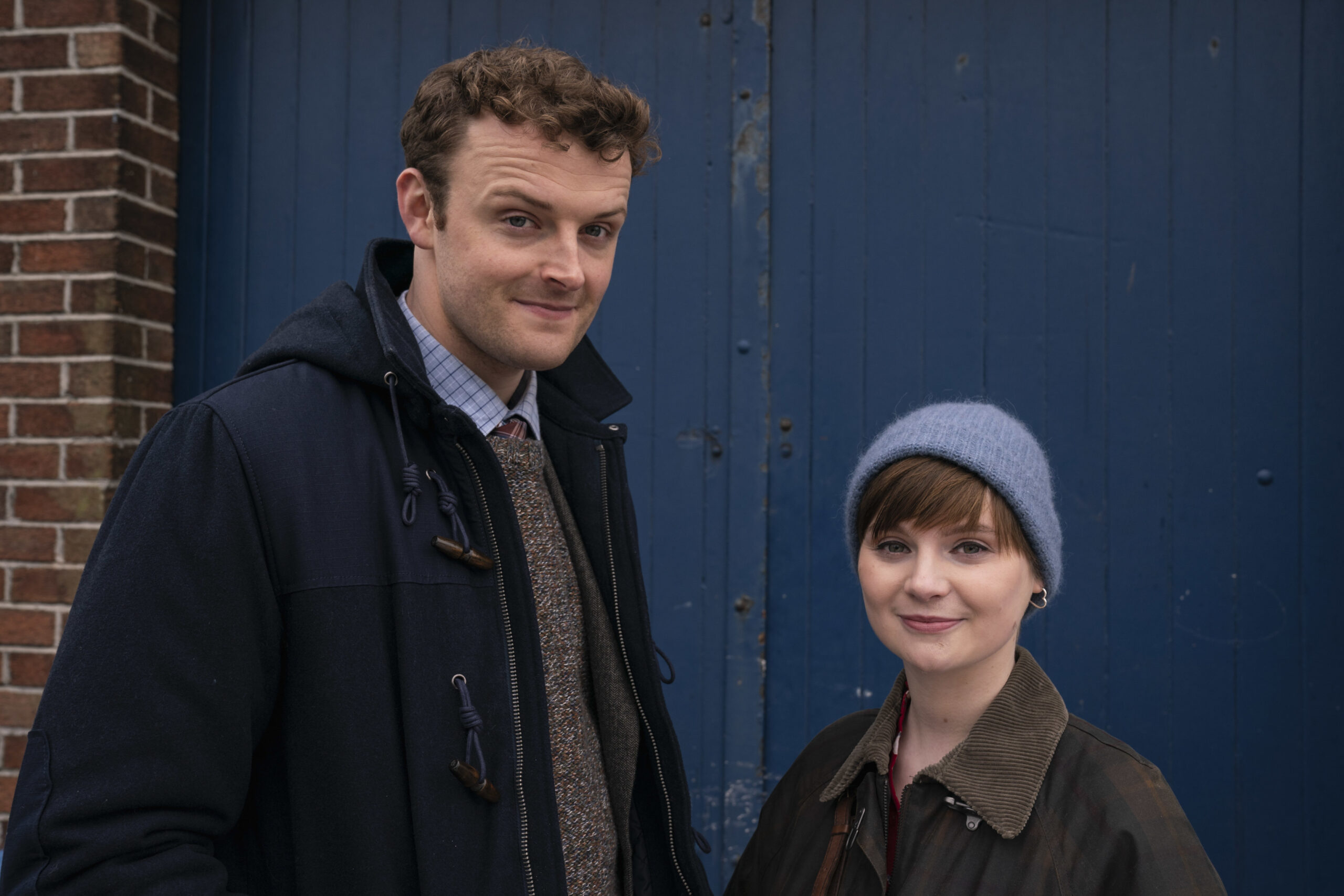  'Birdy' (CHRIS WALLEY) (left), Izzy Brannick (LOLA PETTICREW) (right), they stand outside a blue door with smiles