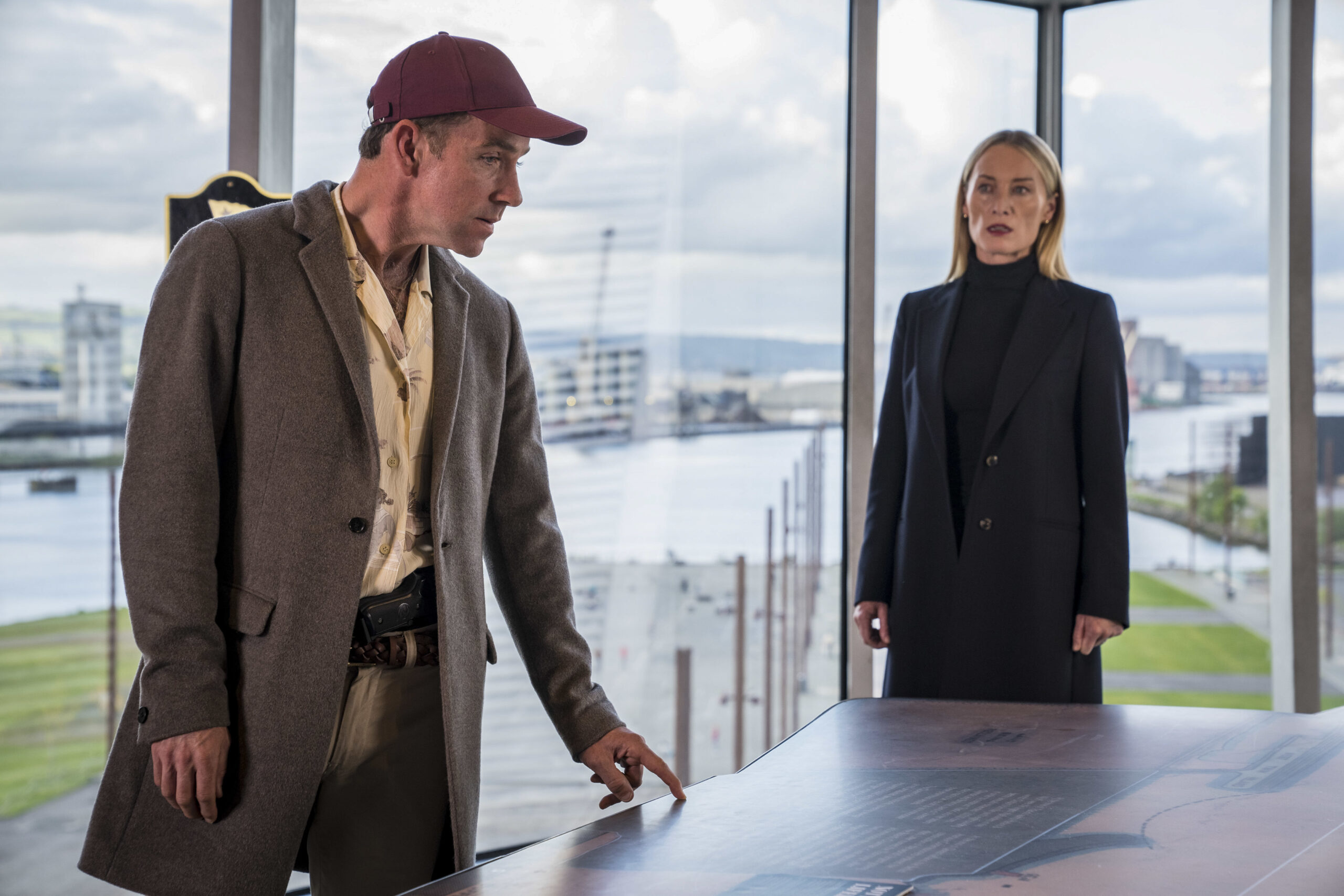 Jonjo O'Neill as Ryan Savage (left) and Victoria Smurfit as Olivia (right) in Bloodlands episode 4, they lean over a table discussing with stressed faces