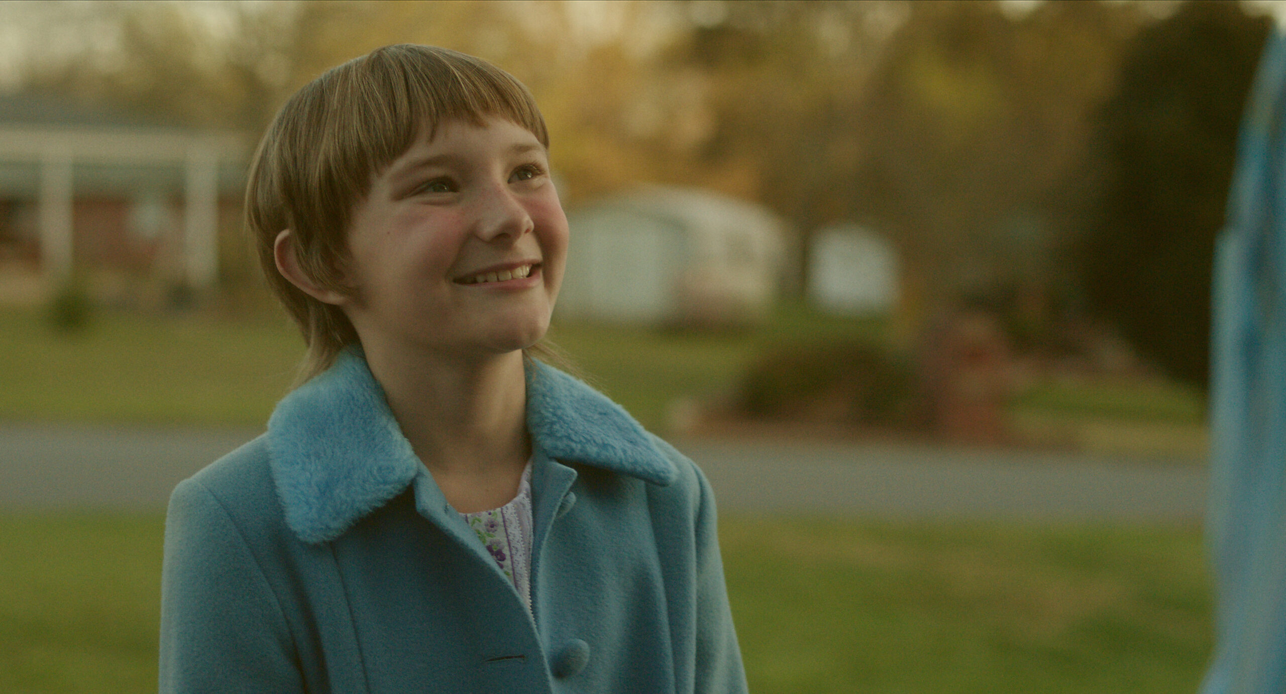 Hendrix Yancey as Jan Broberg in A Friend of the Family, she smiles up at a man outside with a blue coat on