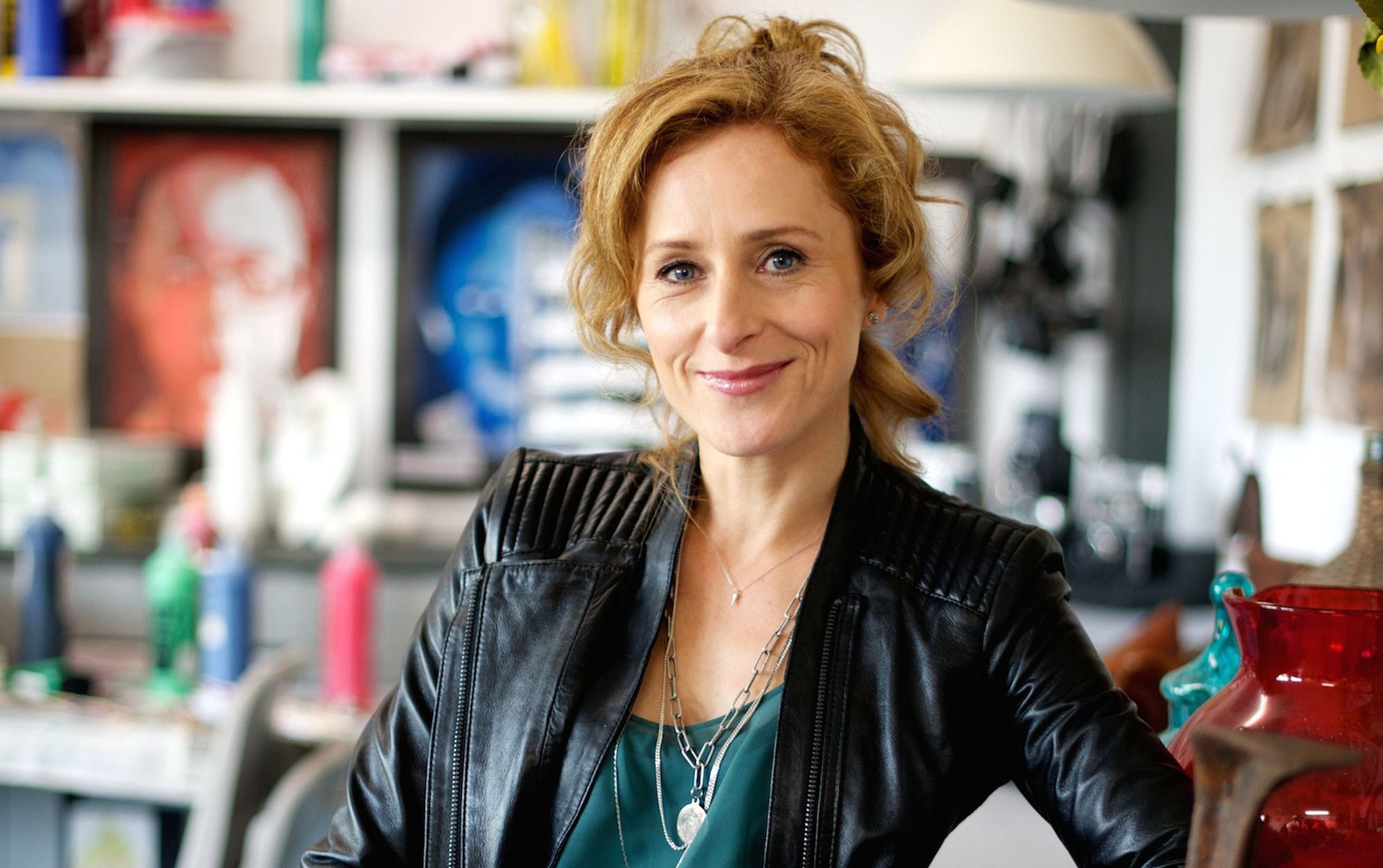 Nicola Stephenson as Allie Westbrooke in Waterloo Road, she smiles in a leather jacket in an art classroom