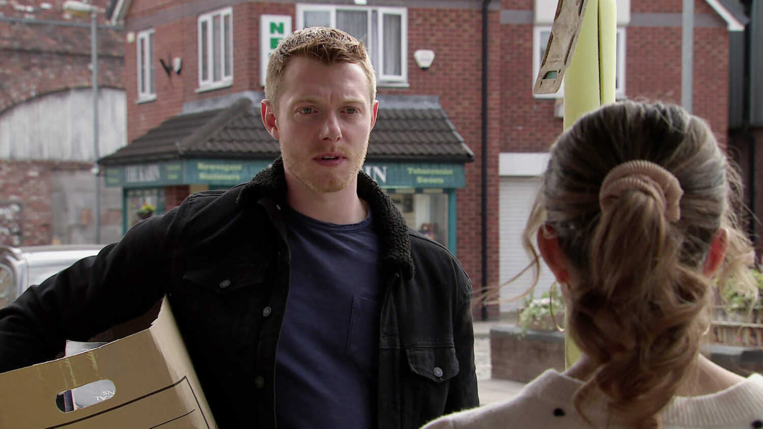 Coronation Street Daniel holding a box, looking concerned