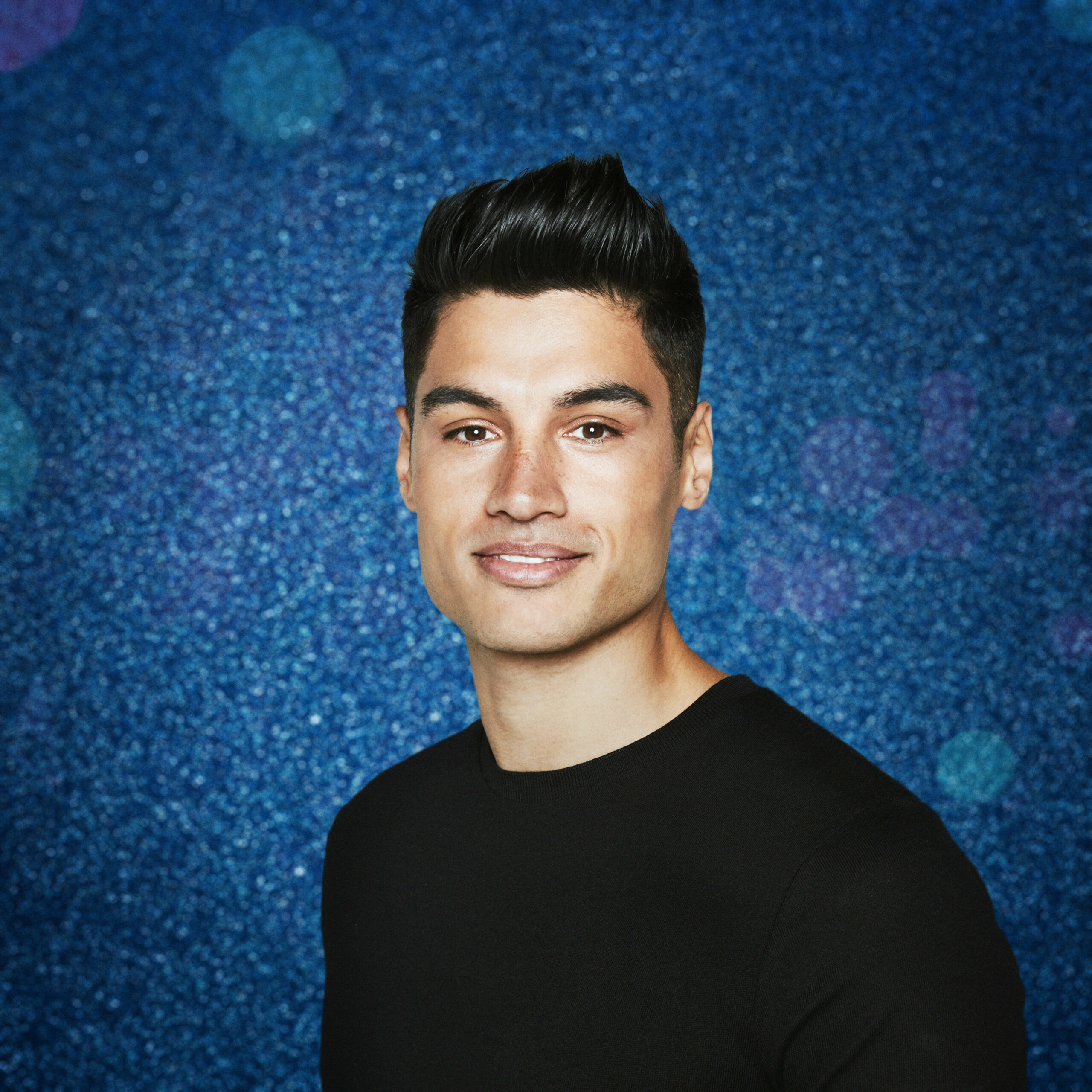 Siva Kaneswaran in front of a blue glitter background