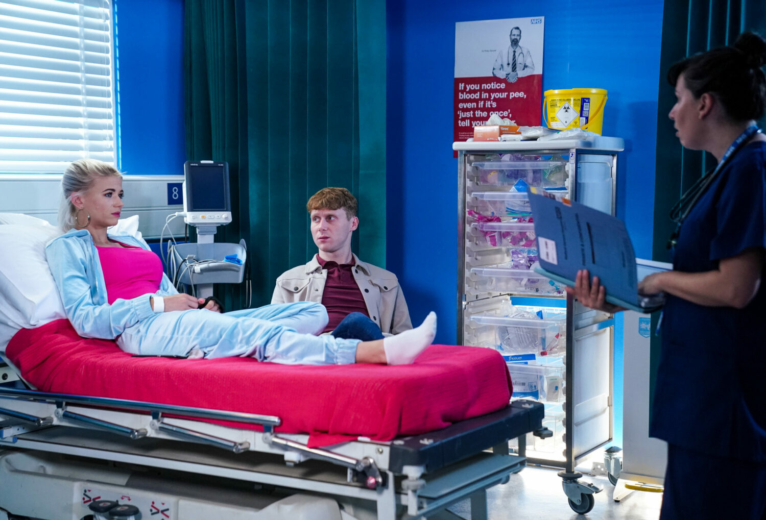 Lola in a hospital bed with Jay and a doctor looking at her EastEnders