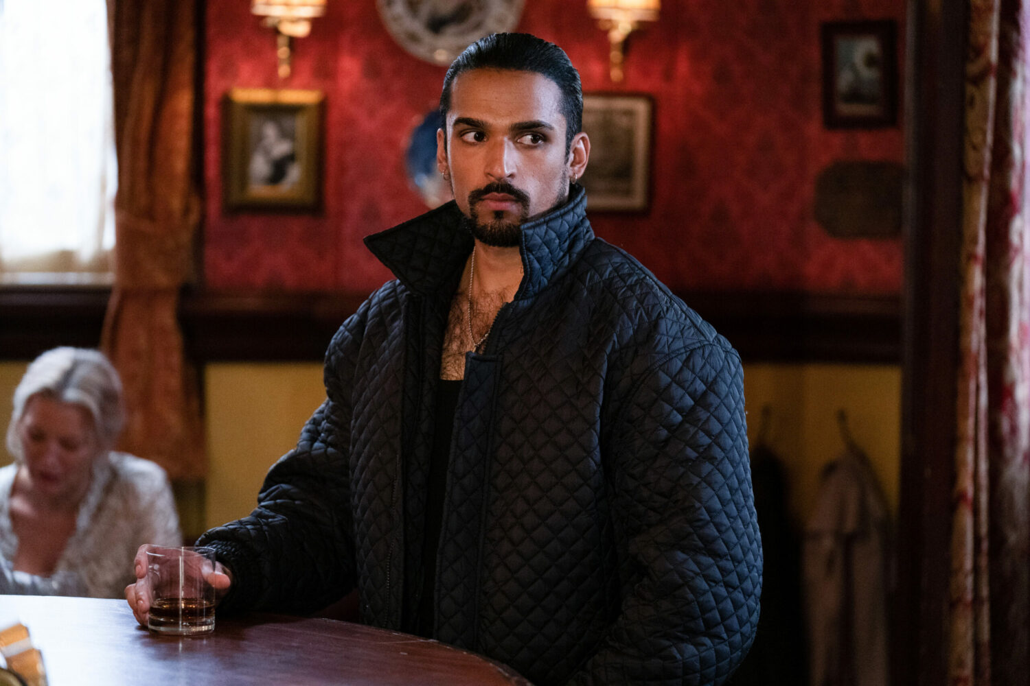Ravi looking suspicious holding a drink in EastEnders in the Vic
