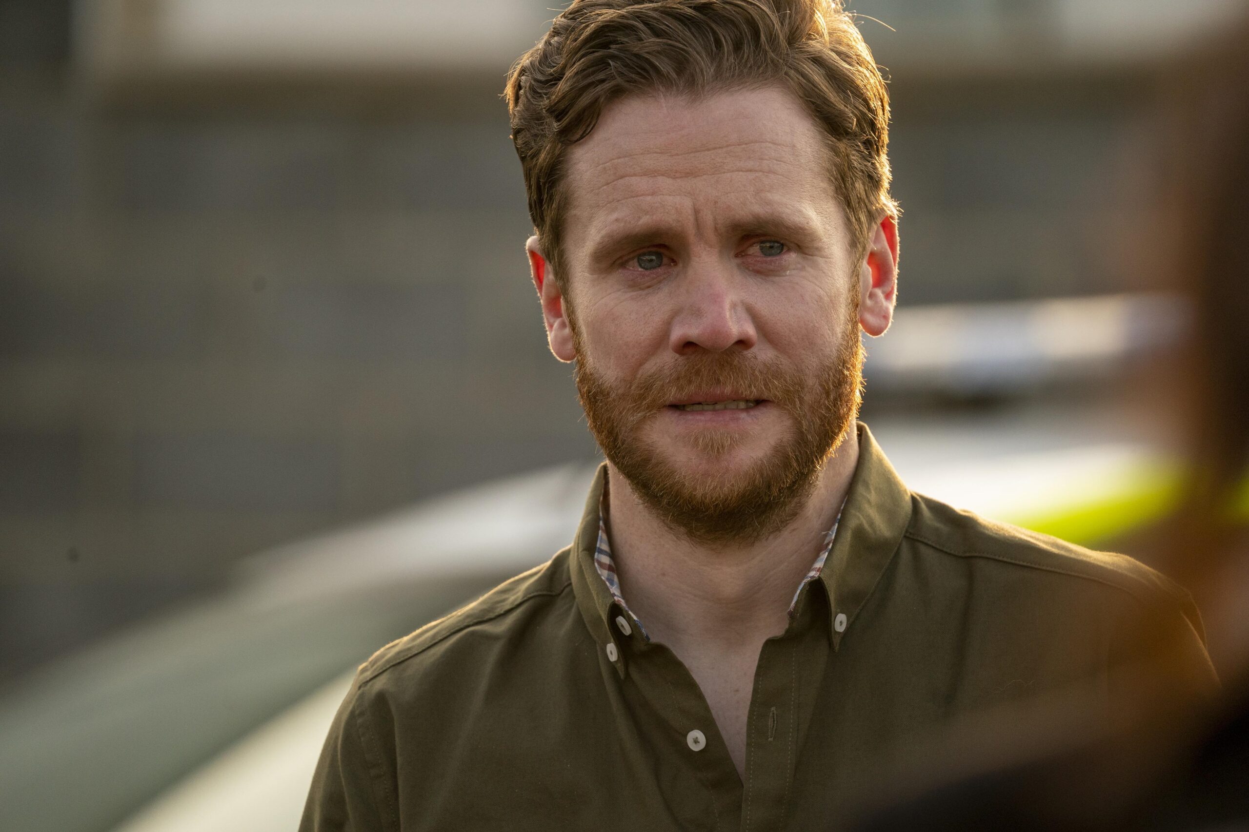 Ian Lloyd Anderson as Owen in The House Across The Street, he looks upset as he stands outside next to a police car