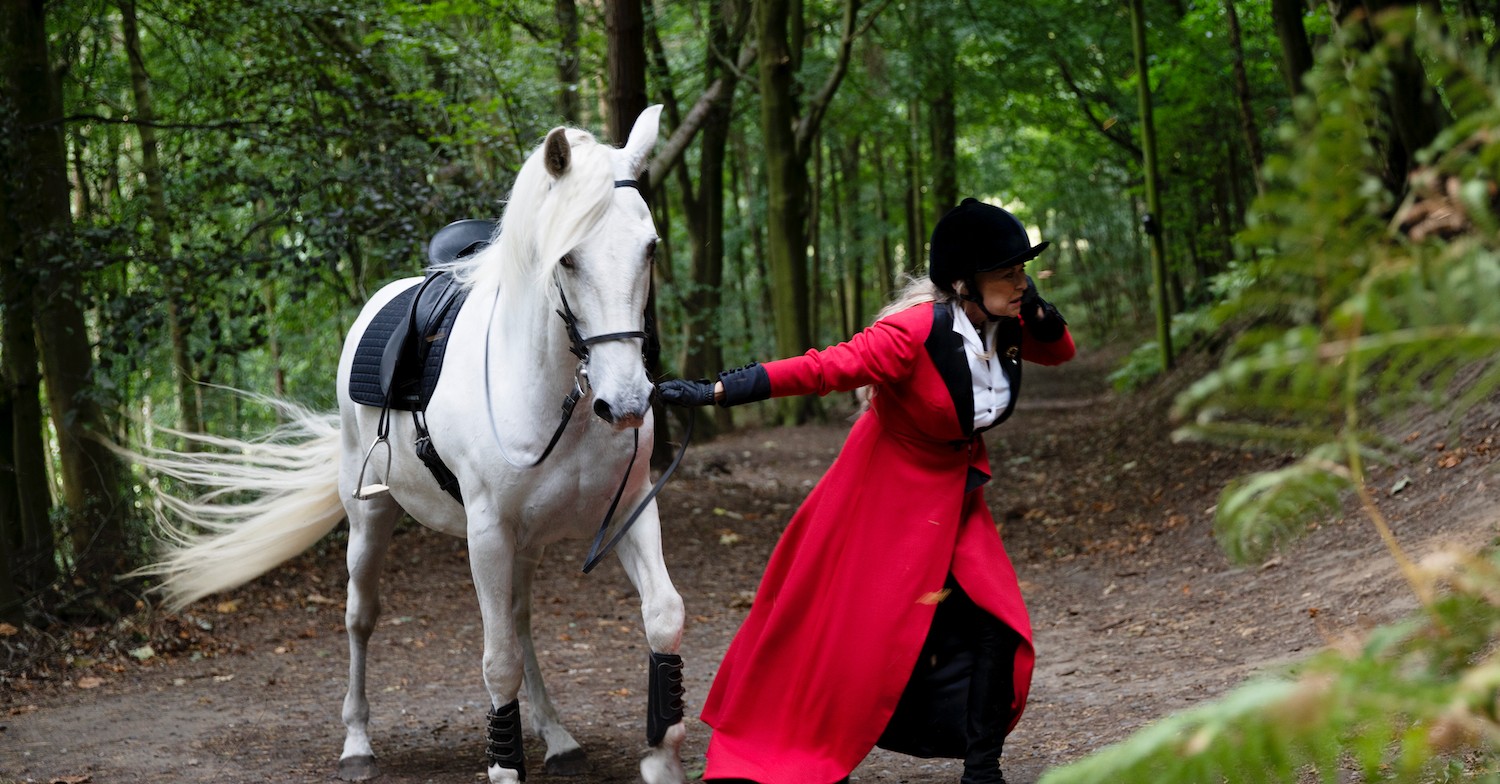 Emmerdale's Kim Tate leading a white horse while wearing a bright red overcoat