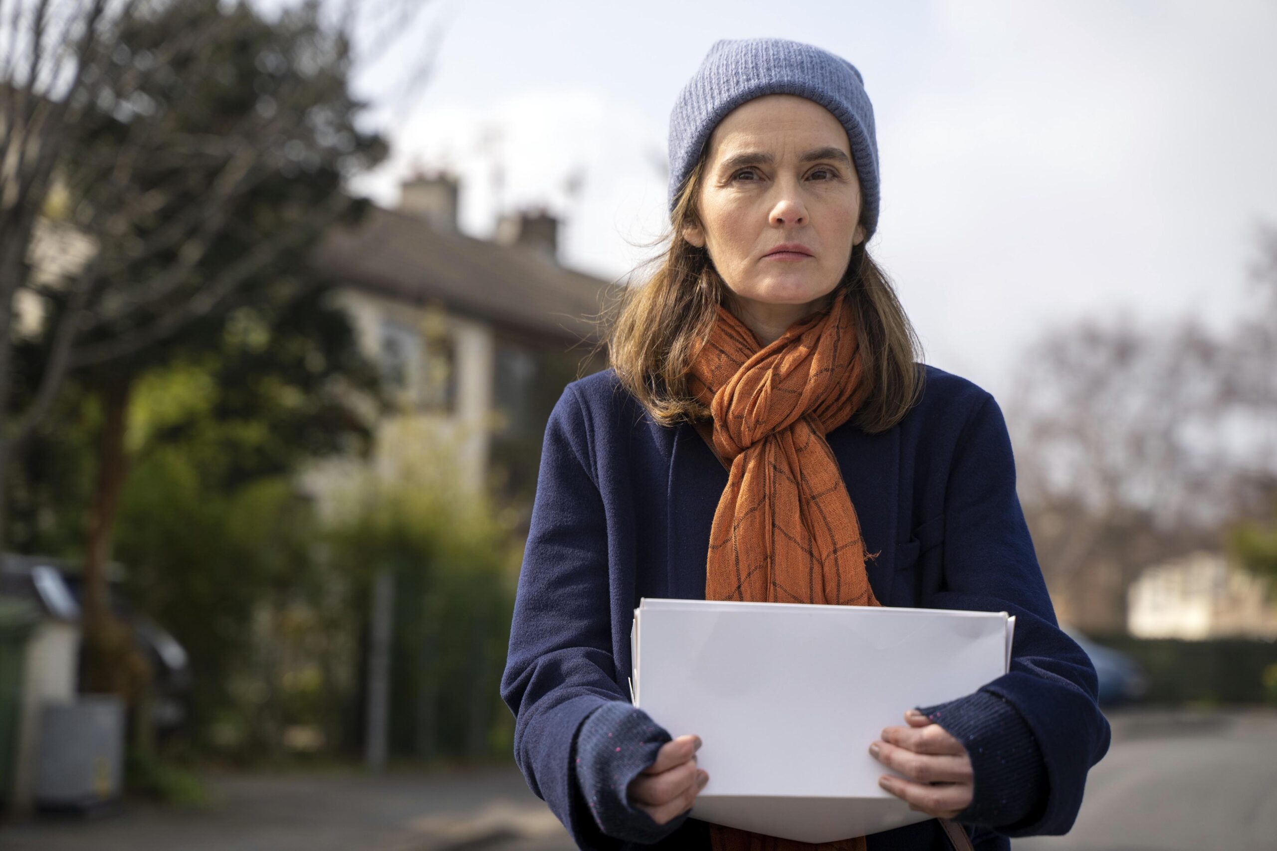Shirley Henderson as Claudia in the house across the street episode 2, she holds up white pages with a concerned expression, standing outside