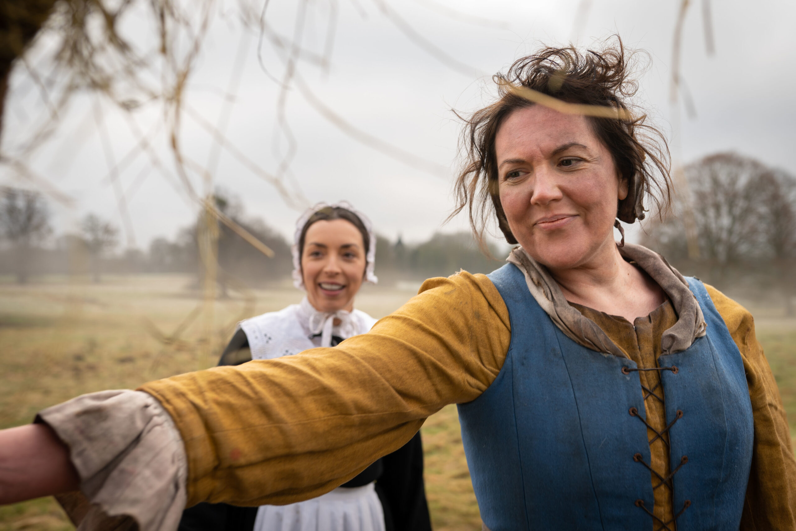 Katy Wix as Mary in Ghosts, she points to her left as Annie stands behind her smiling