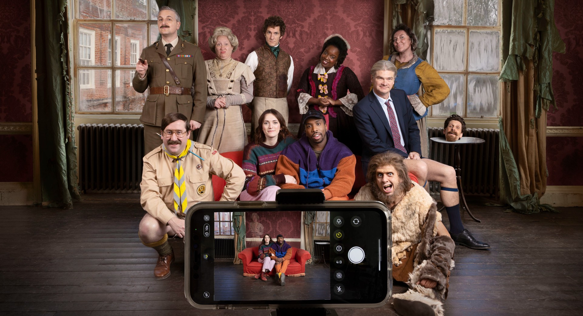 The cast of Ghosts pose and smile at a phone