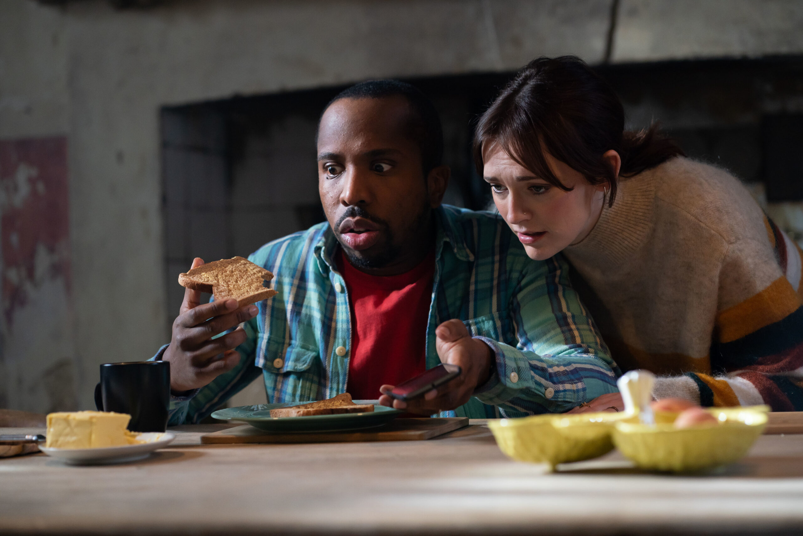  Mike (KIELL SMITH-BYNOE), Alison (CHARLOTTE RITCHIE) in Ghosts, they lean over a table looking at toast with intense expressions